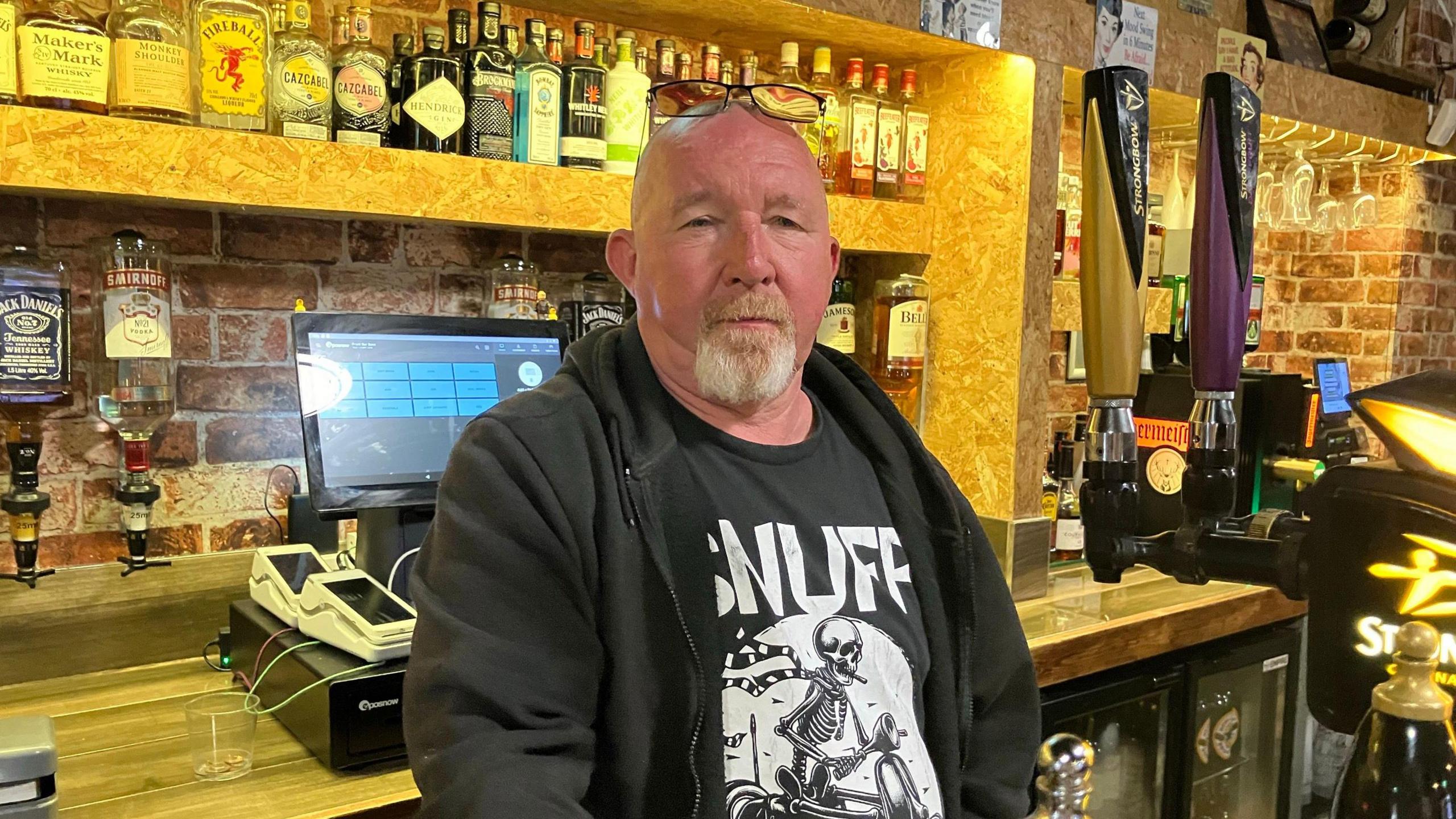 Paul Keenan stood behind the bar - glasses perched on the top of his head wearing a black hoody. 