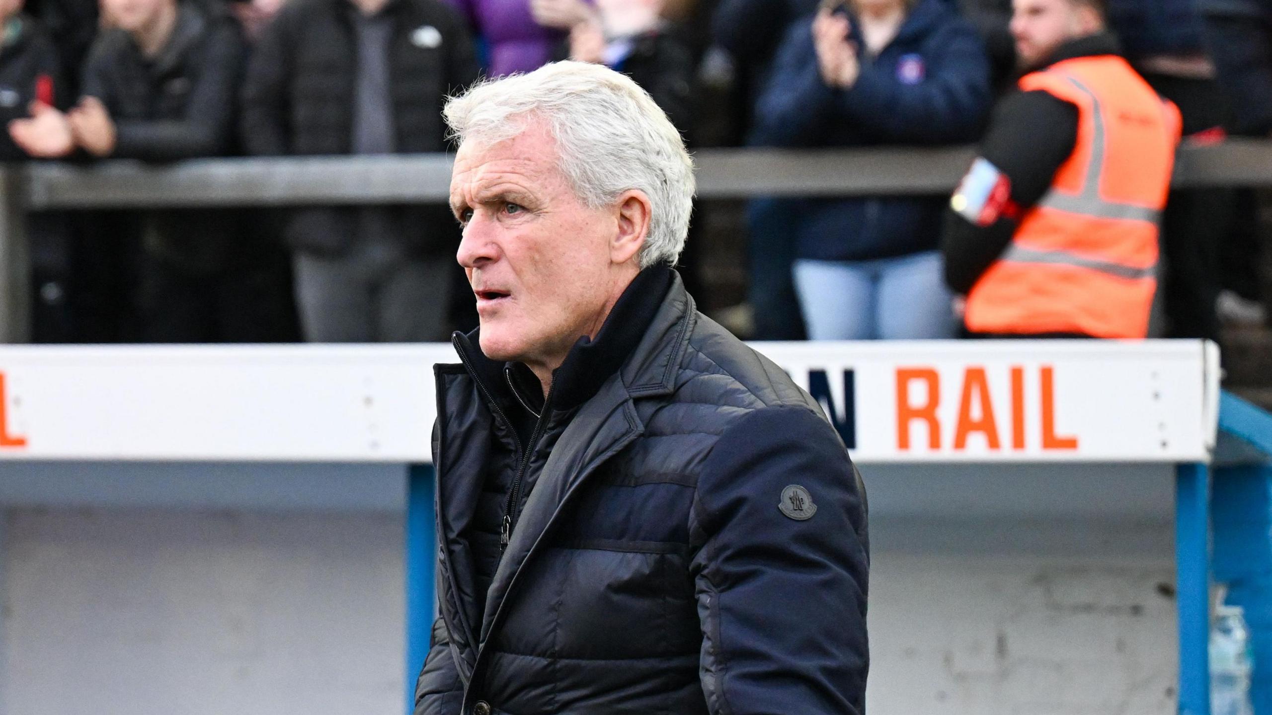 Mark Hughes, wearing a thick coat, stood in front of the dugout at Brunton Park