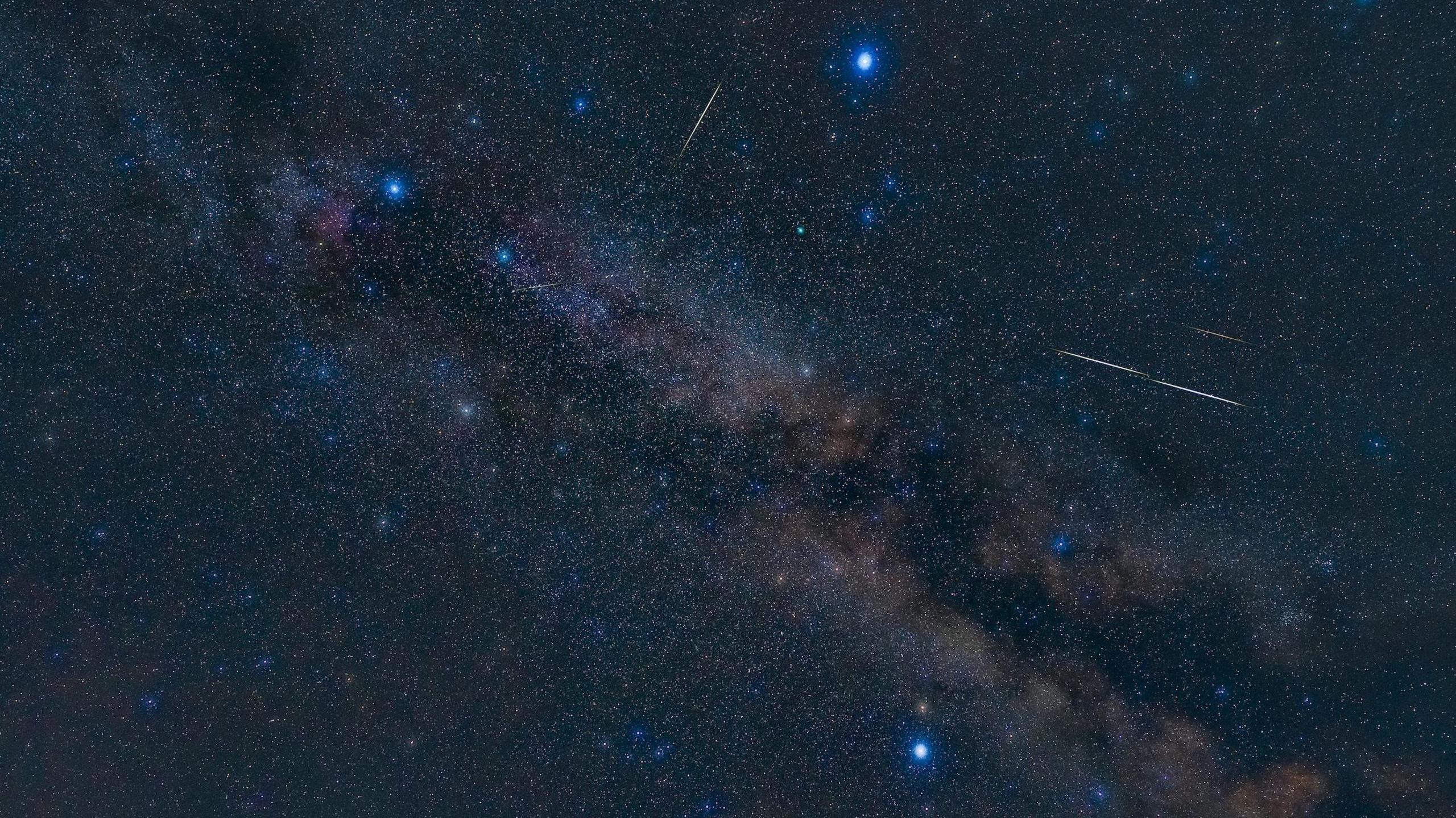 A picture of the night sky showing the three stars in the summer triangle. A meteor shower surrounds the stars.