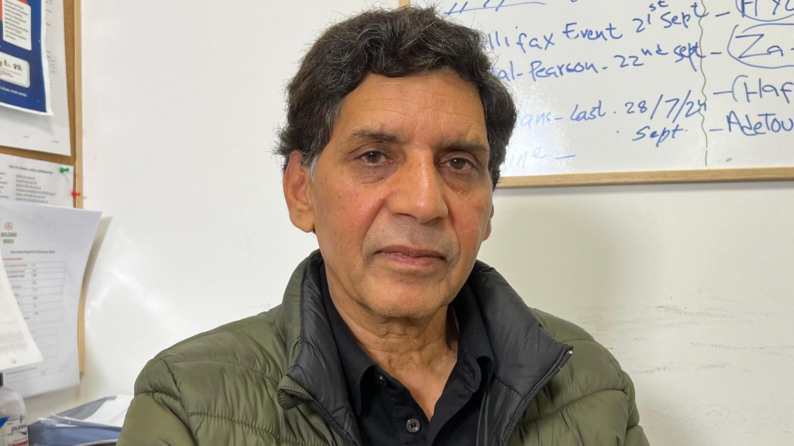 Head-and-shoulders shot of Bashir Siraj, who has thick short black hair, greying at the temples, and is wearing a khaki-coloured jacket over a black shirt