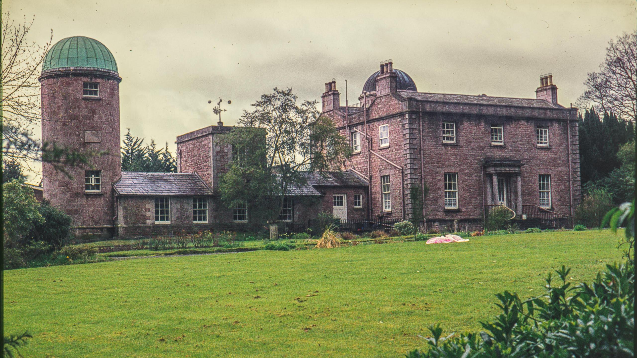 A digitalised photo from a film of a reddish building, it has a green sphere top on the left of the building.