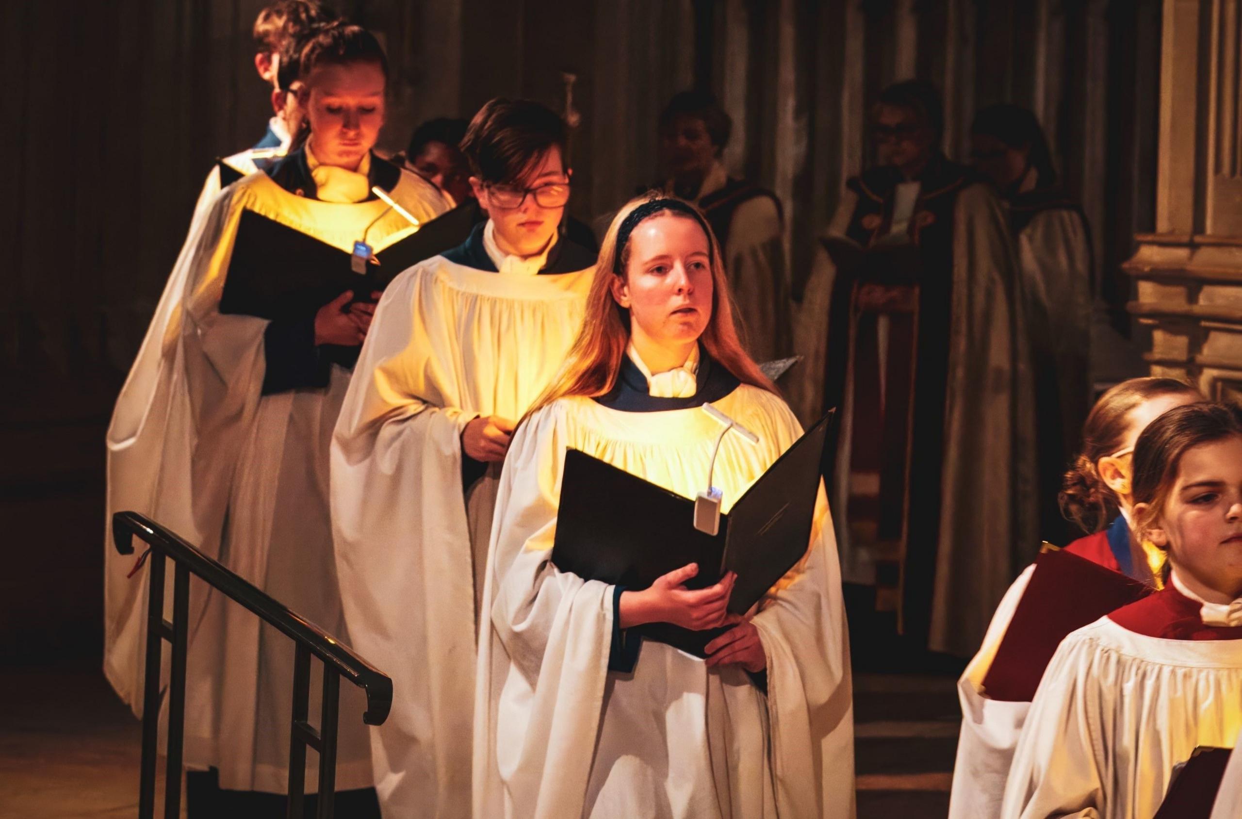 Female choristers in white robes walk through Gloucester Cathedral as part of a Candlemas service