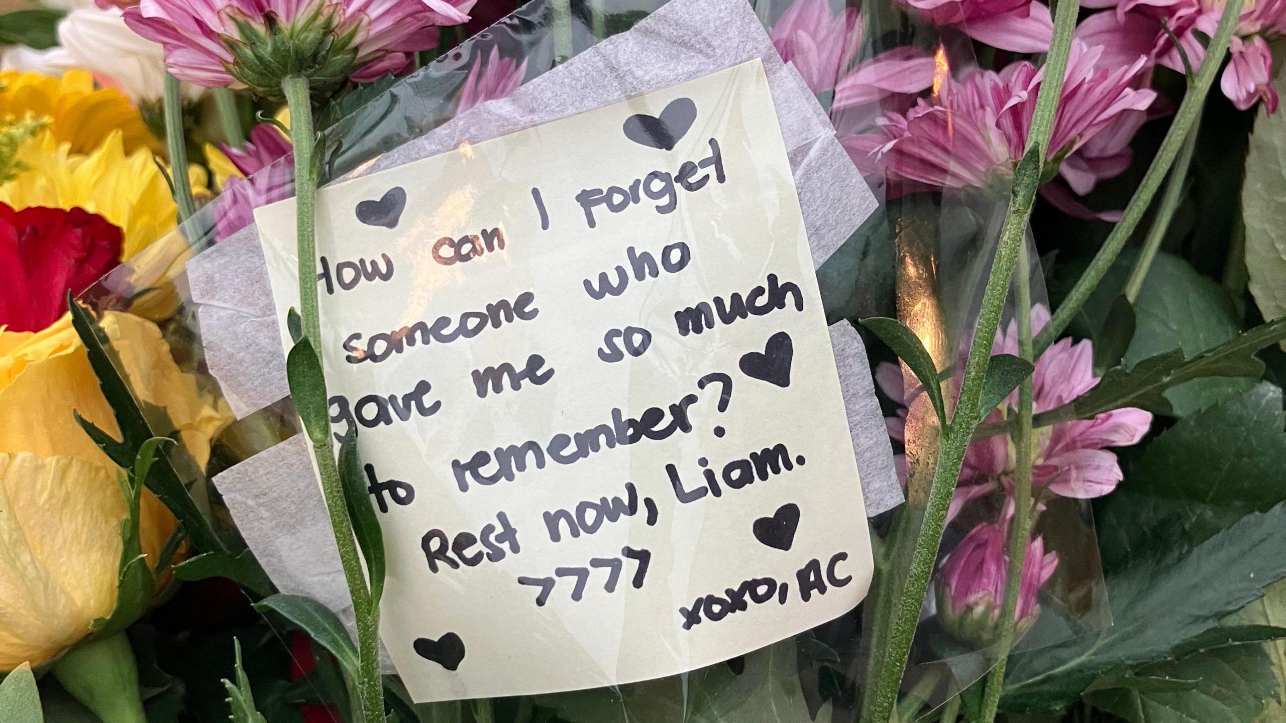 A note in a bouquet of flowers. It is dedicated to Liam Payne. It reads: "How can I forget someone who gave me so much to remember? Rest now, Liam".