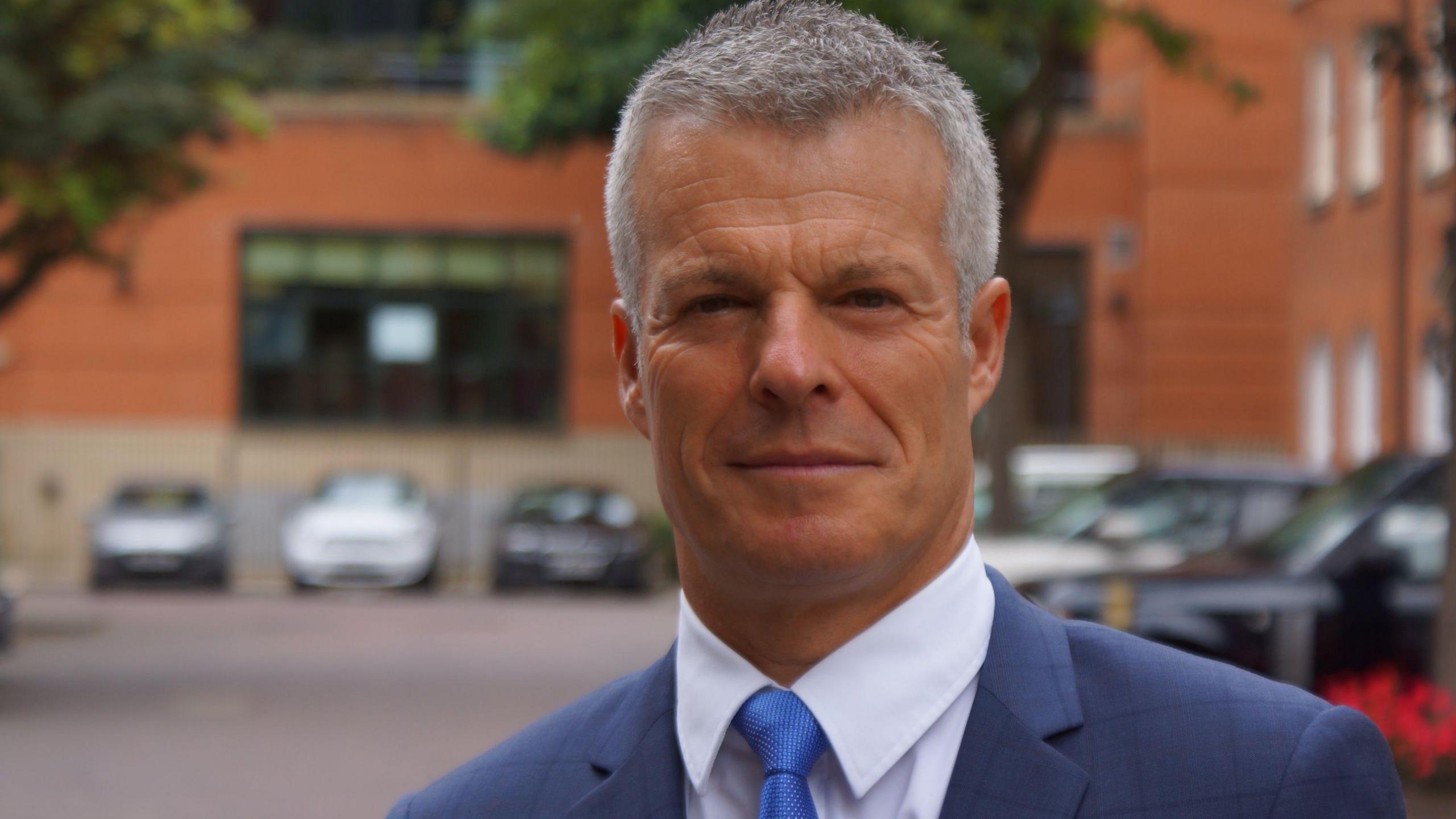 Nick Freeman stands in a carpark wearing a suit and blue tie