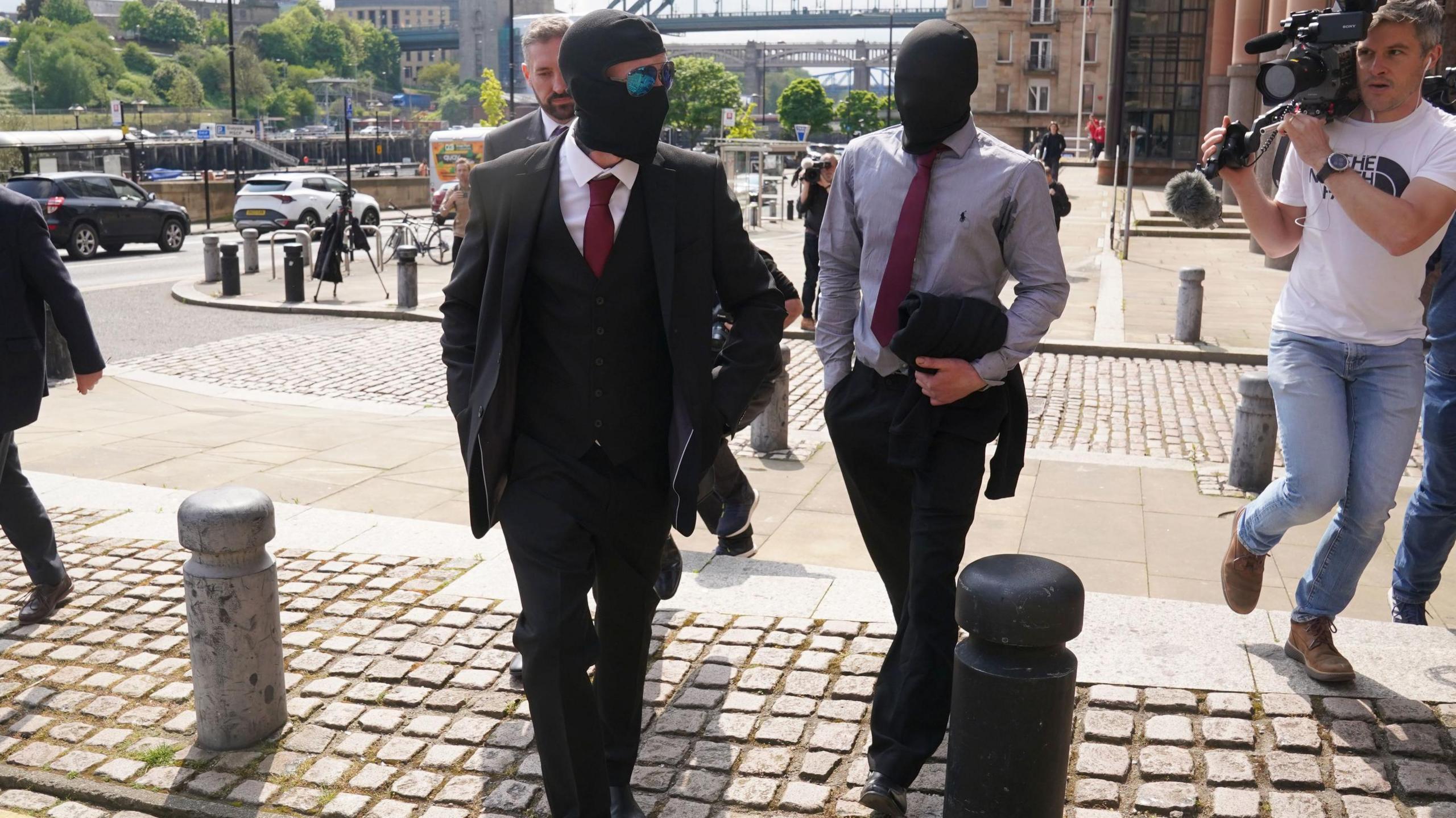 Daniel Graham and Adam Carruthers are walking into court but they have covered their faces with balaclavas. A man with a camera is walking alongside them.