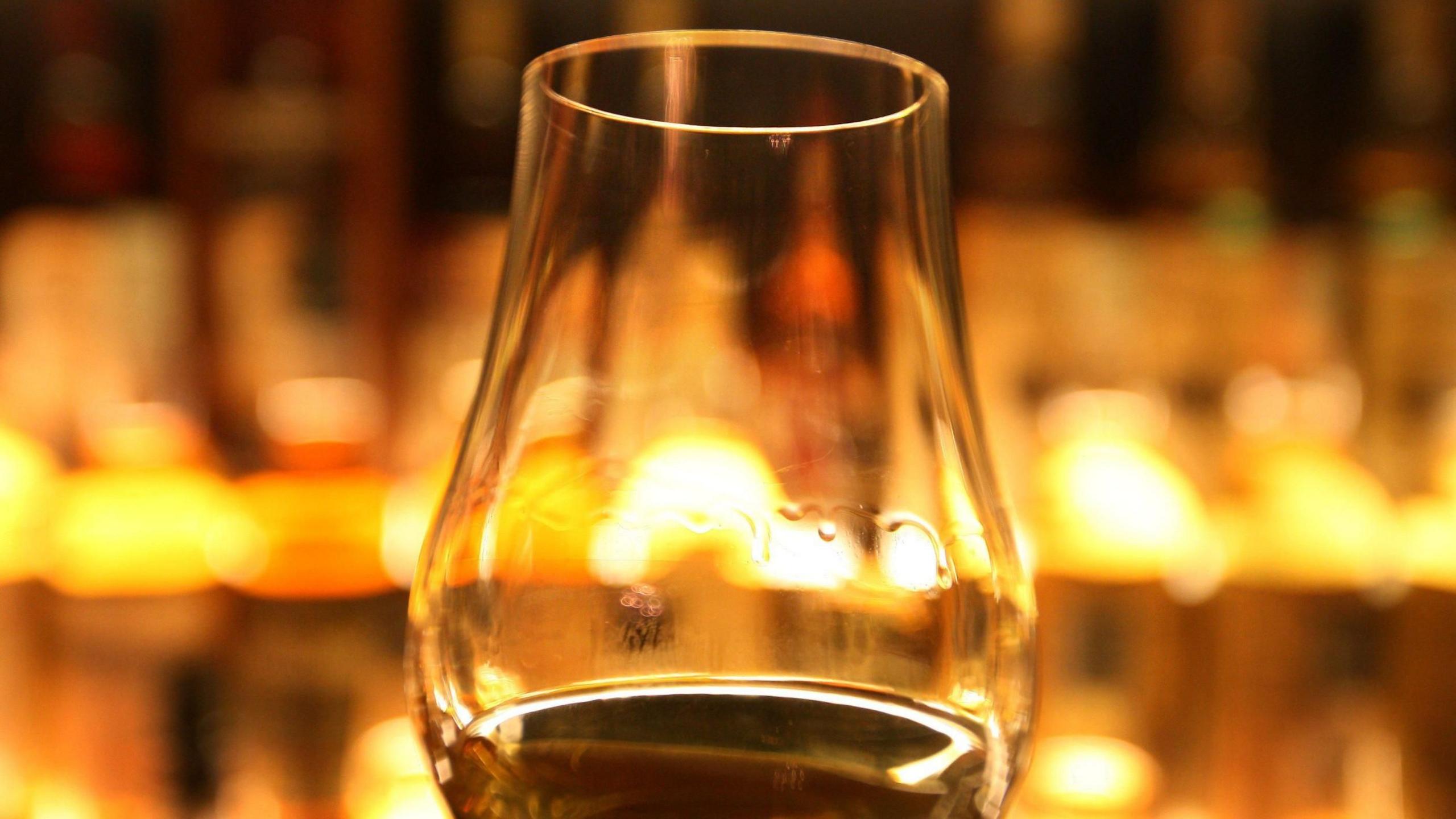 A glass of Scotch whisky with yellow lights behind it
