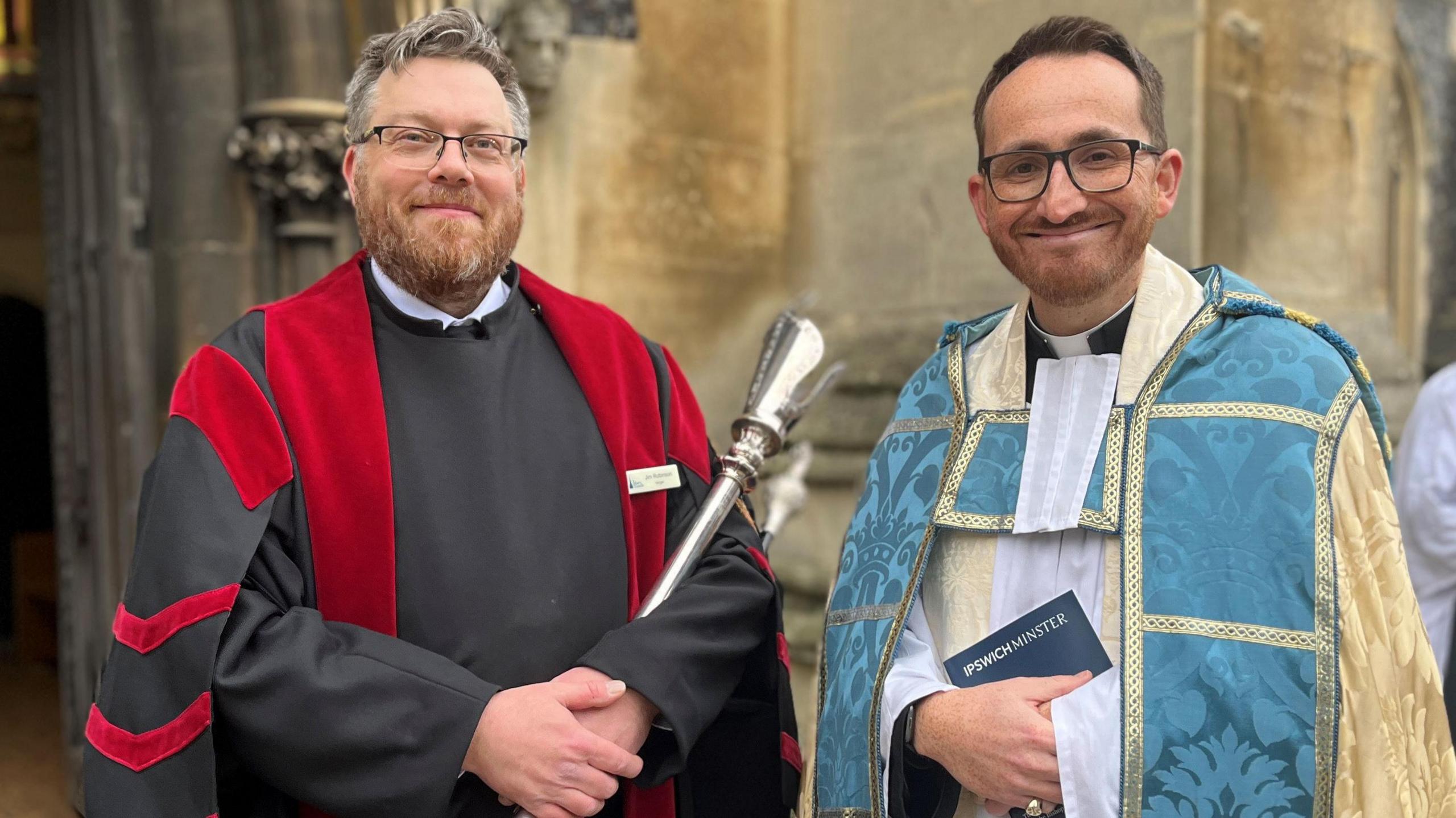 Jim Robinson, verger at Ipswich Minster, and Revd Tom Mumford, both dressed in Anglican church robes, stand outside St Mary Le Tower church