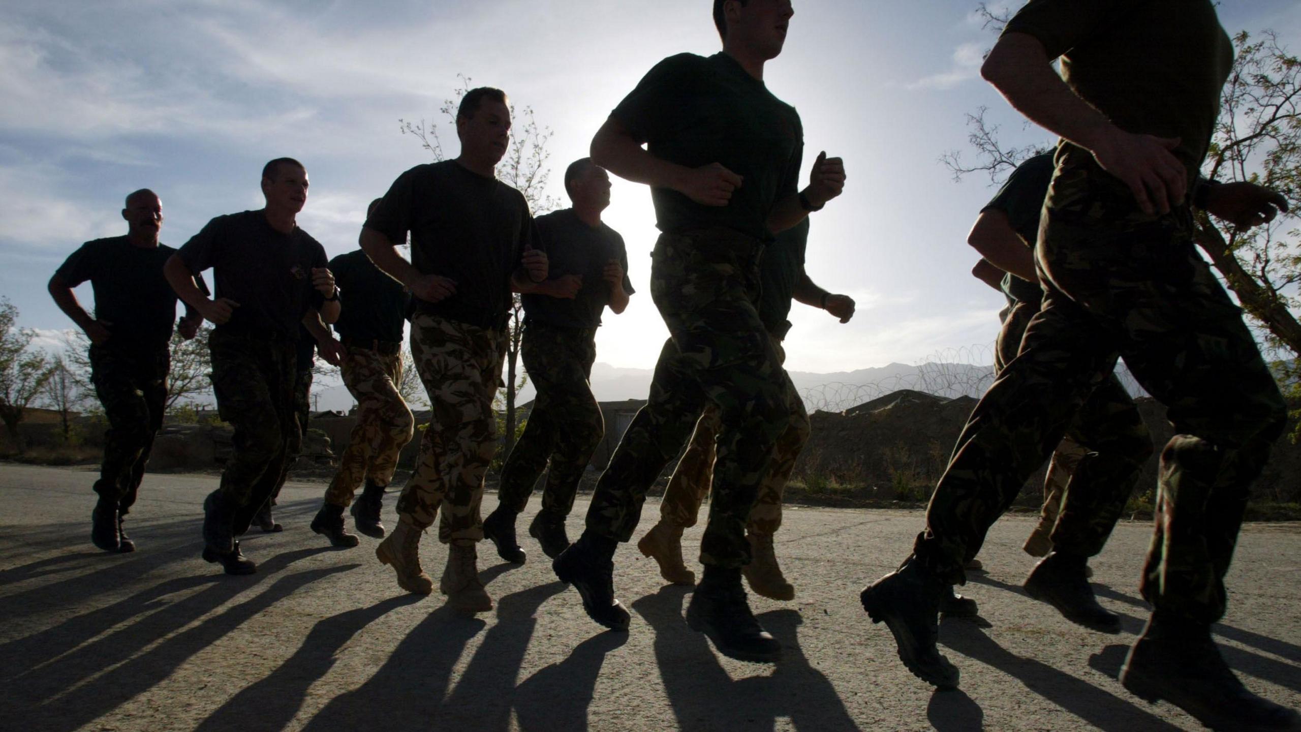 Service people in uniform running along a pavement with the sun behind them