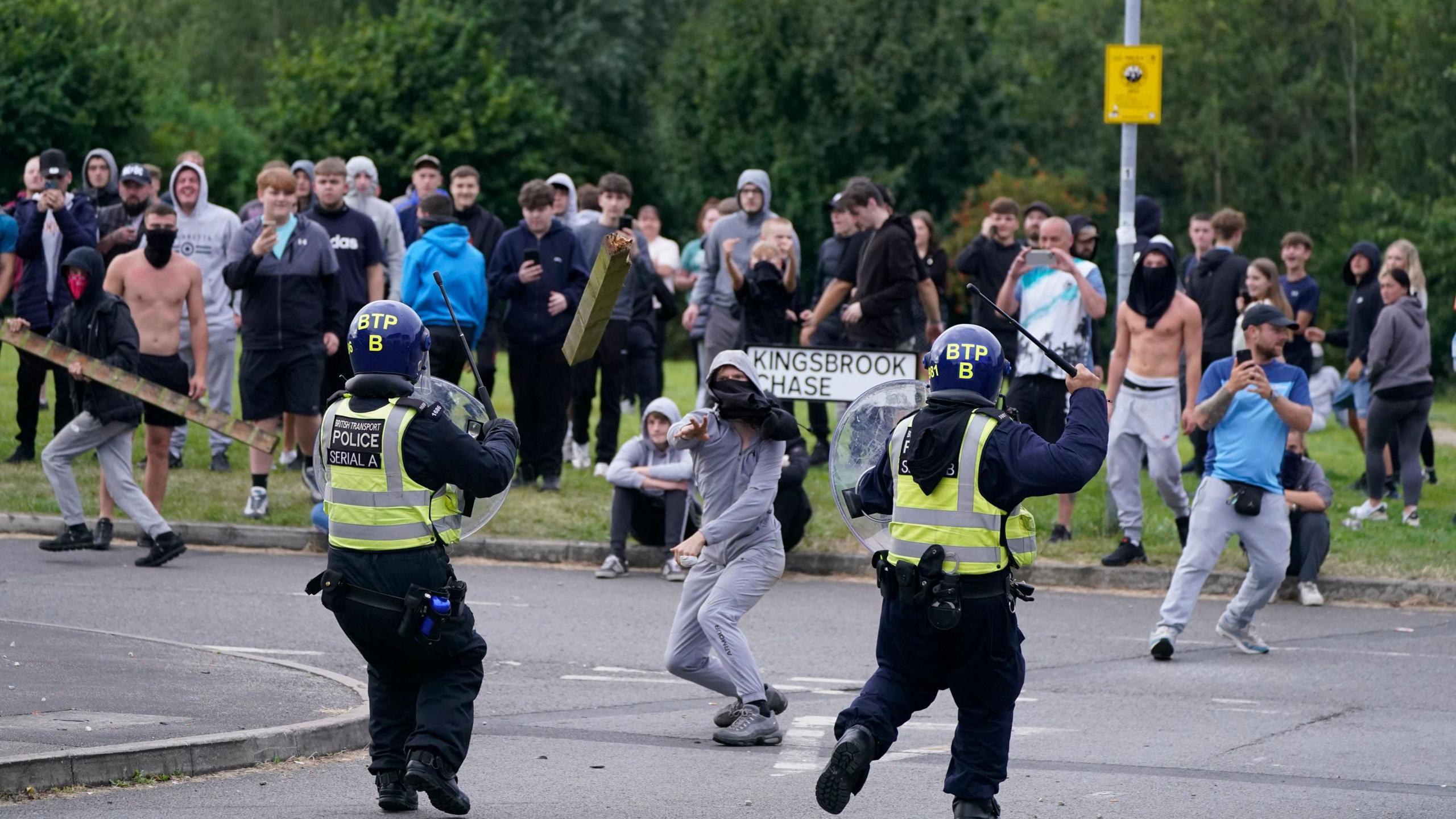 A man throws a fence post toward police officers during demonstrations