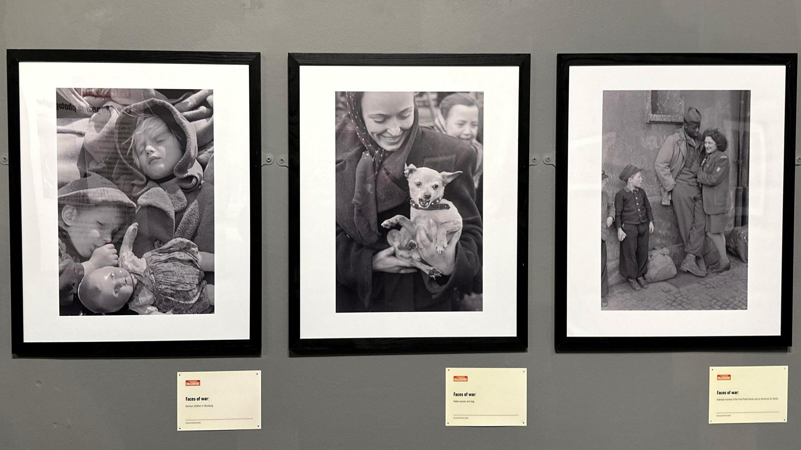 There framed photos on a wall featuring children holding a doll, a woman holding a small dog, and a man and a woman standing against a wall next to a child.