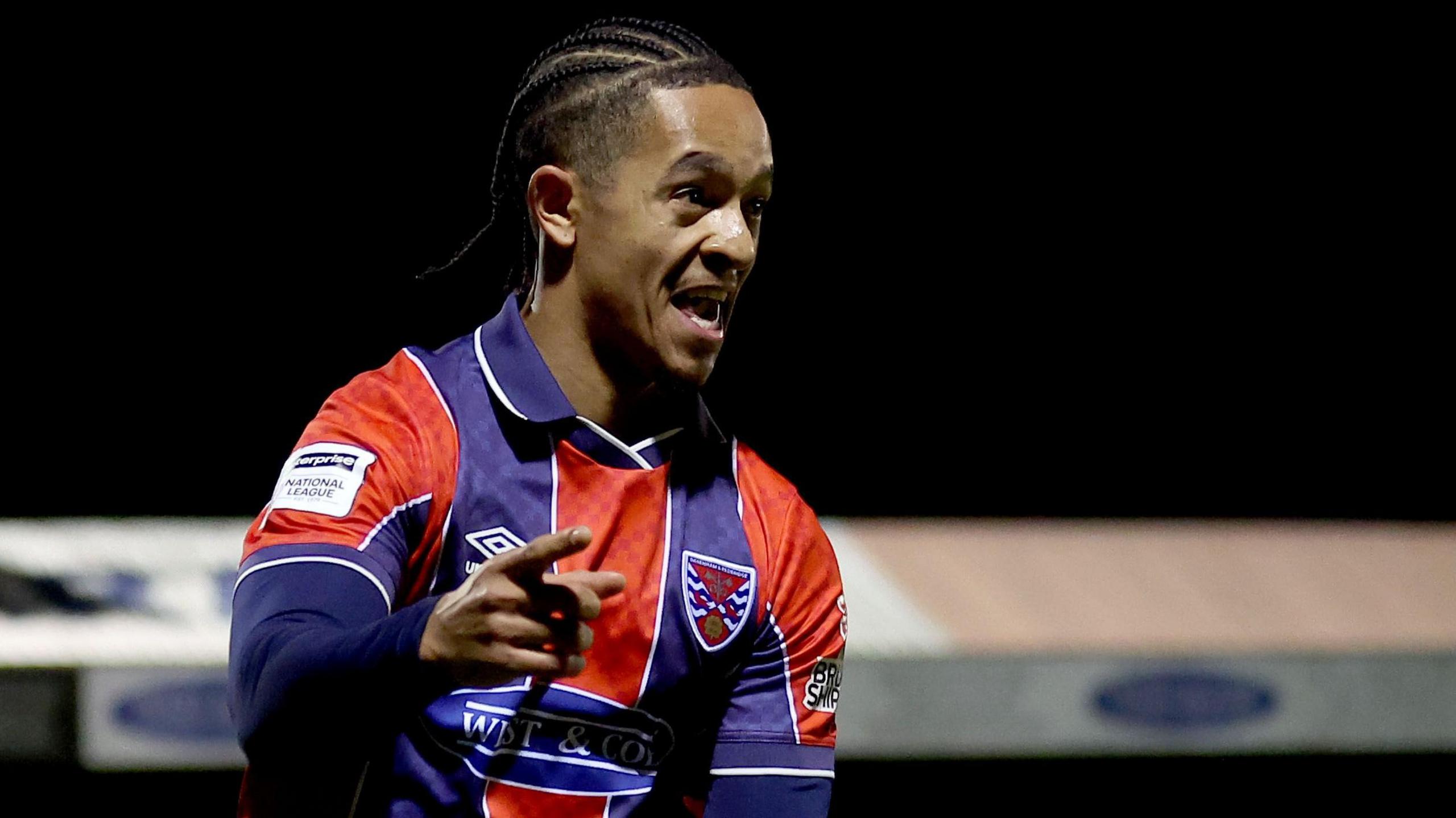 Conor Lawless, wearing a red and blue striped shirt of Dagenham & Redbridge, celebrates scoring against Hanwell Town in the FA Trophy