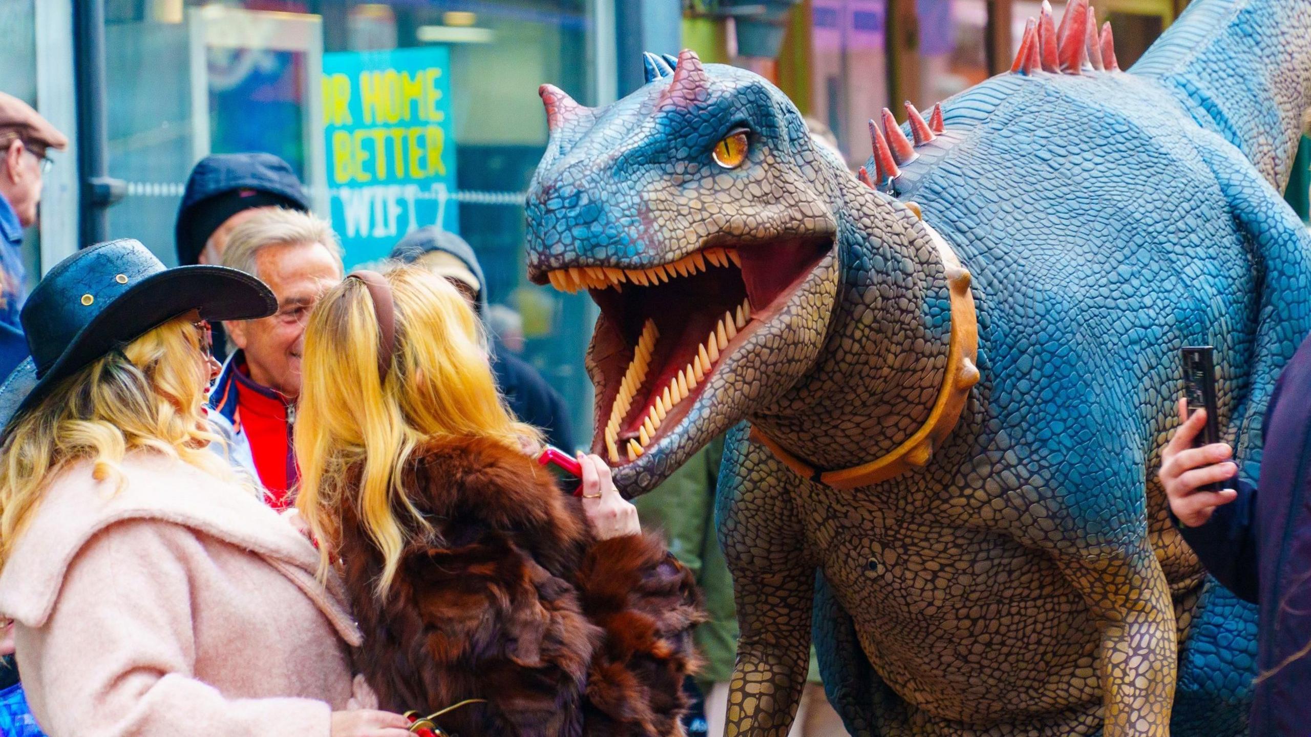 An animatronic dinosaur roars in the face of a blonde woman,