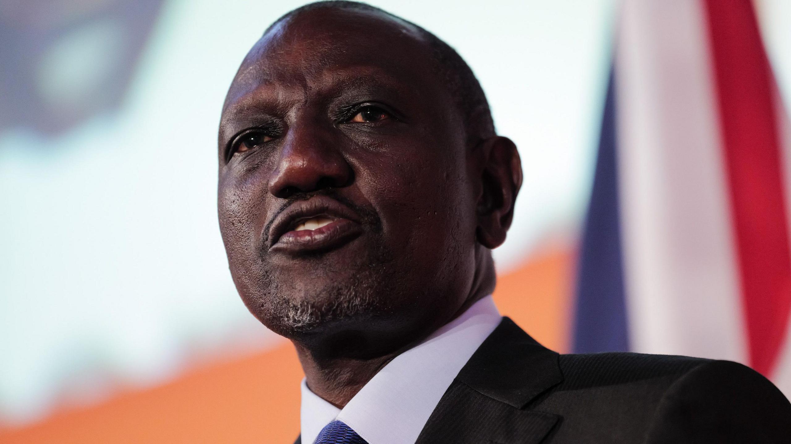 William Ruto, in a black suit, white shirt and blue tie