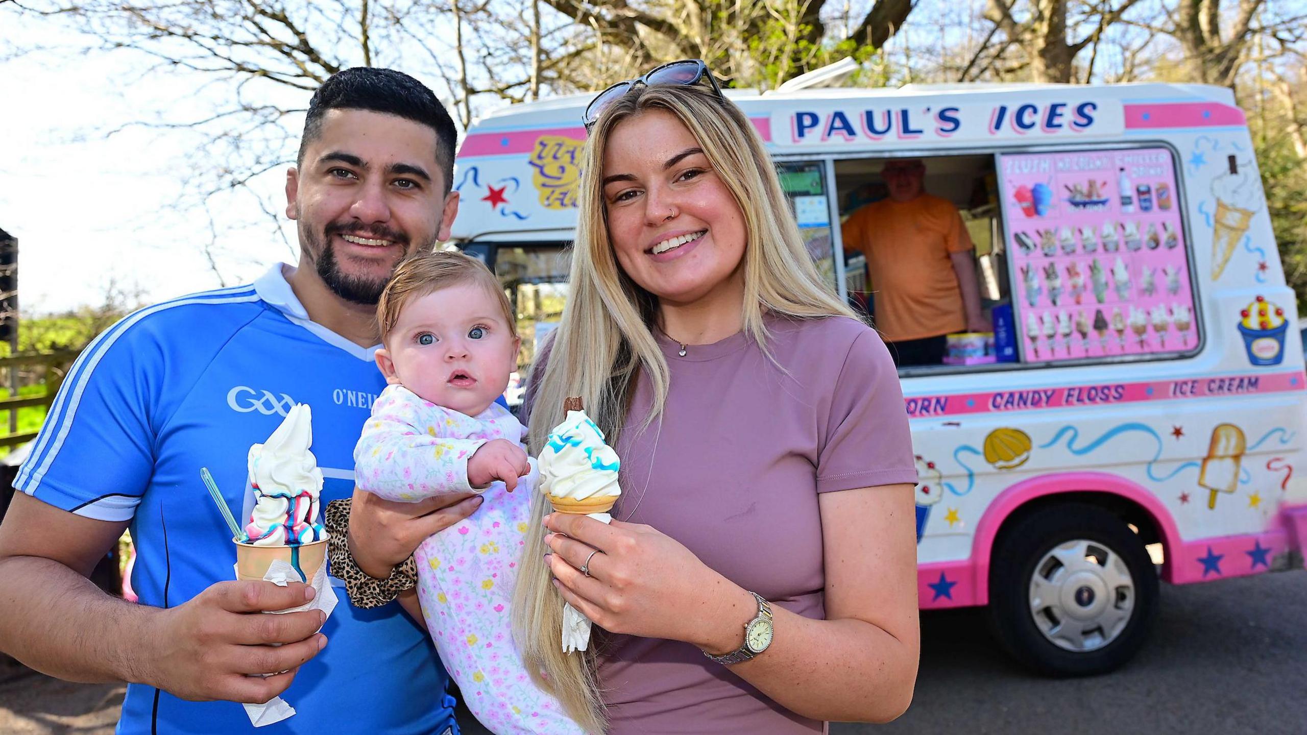 Emma Moore, six-month old Bella and James O’Hare pictured enjoying a ice cream at Shaws Bridge in Belfast in early April. Emma has long, straight blonde hair and is wearing a purple t-shirt and sunglasses. James has dark short hair and a dark beard. He is wearing a blue GAA top. Bella has short, blonde hair and blue eyes and is wearing a white patterned baby grow.