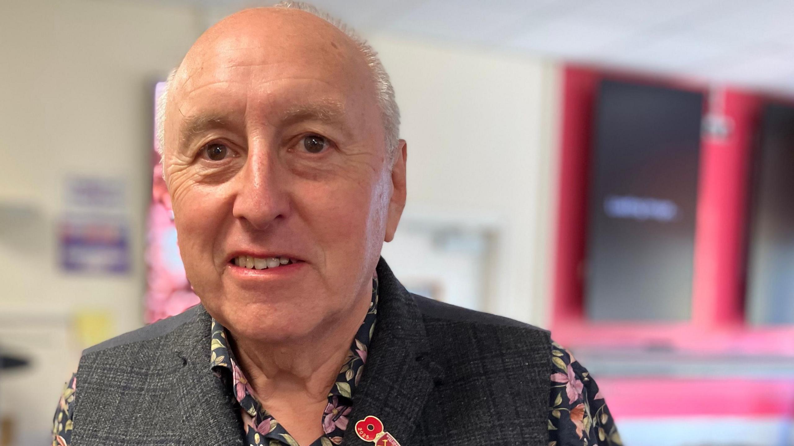 A man with a waistcoat and a floral undershirt, he has a west ham united pin and a poppy