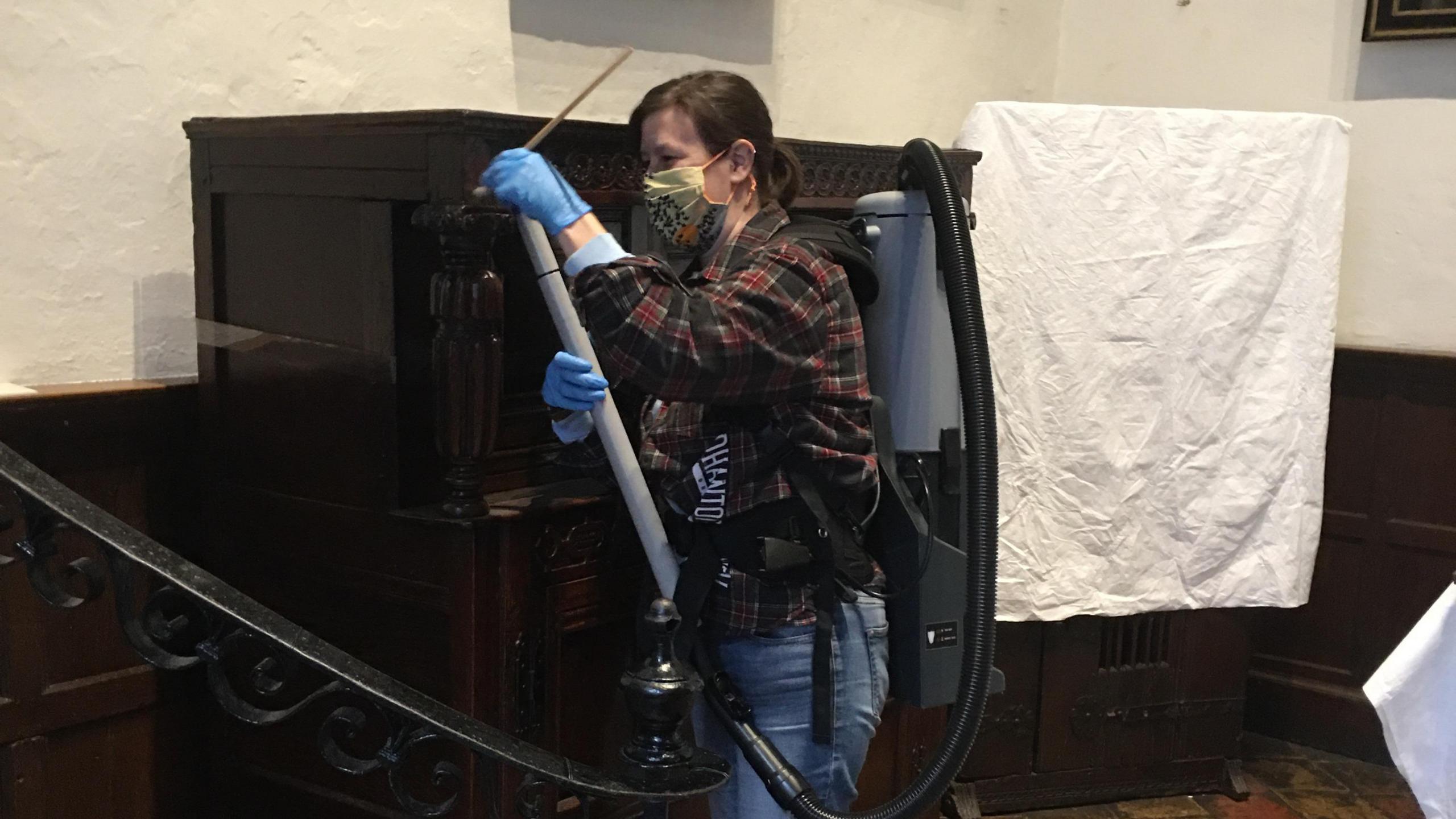 A person cleaning furniture at Strangers’ Hall Museum