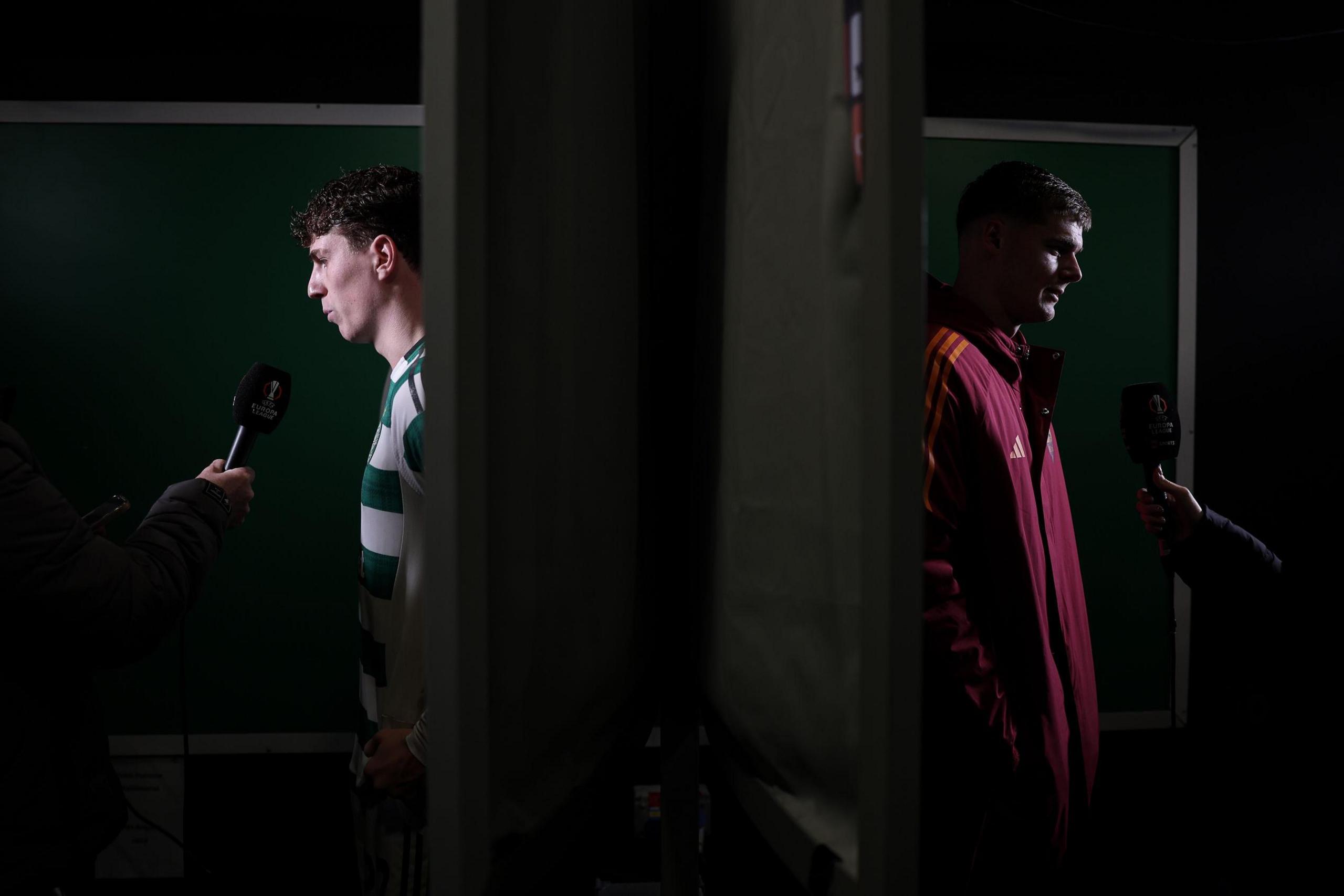 Dos jugadores de fútbol se encuentran en zonas de entrevista separadas por una mampara, cada uno hablando por un micrófono sostenido por un reportero. La escena está tenuemente iluminada, con fondos verdes detrás de ambos jugadores.