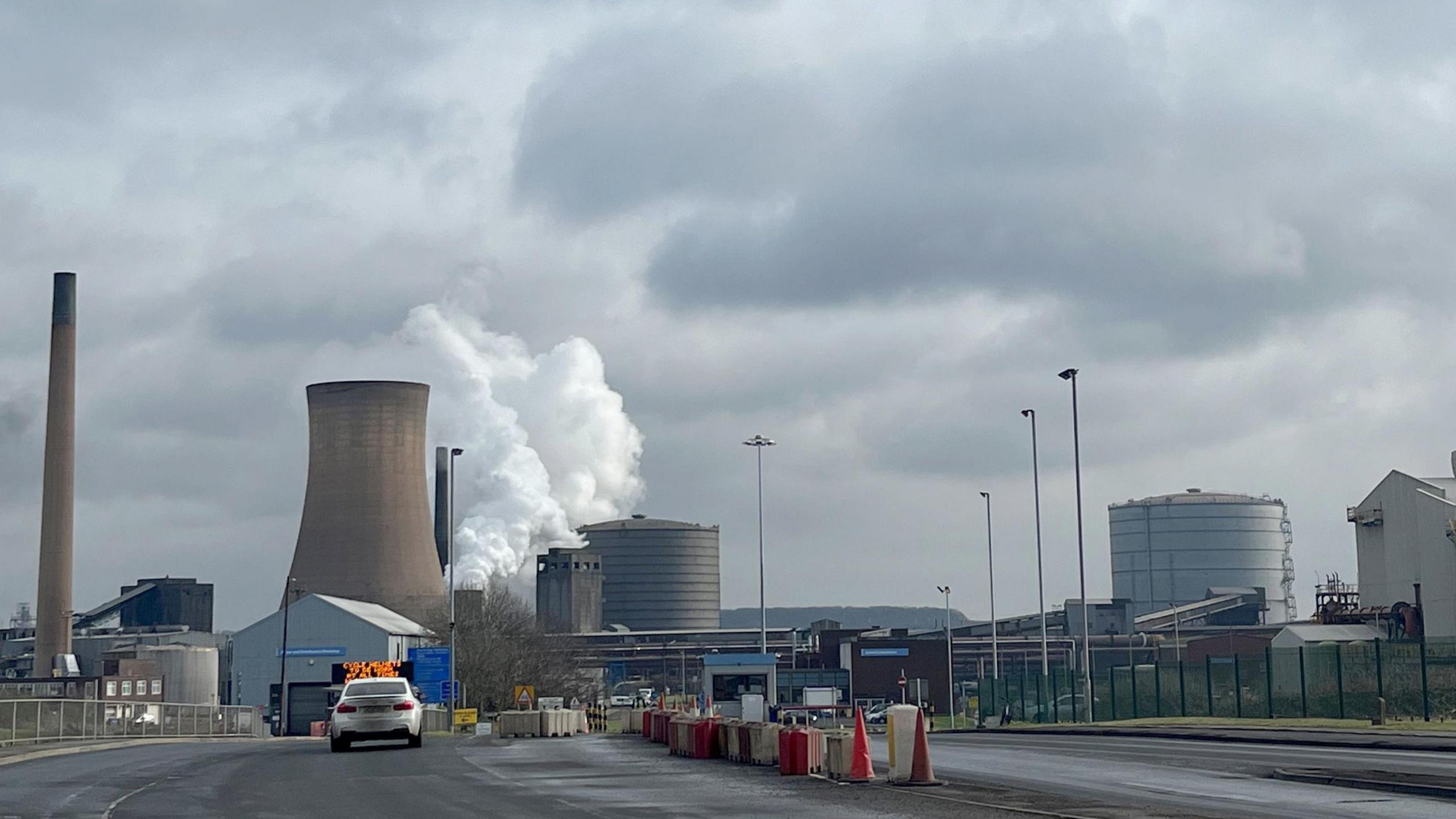 British Steel in Scunthorpe, with cooling towers and production facilities in view, as well as an entrance gate.