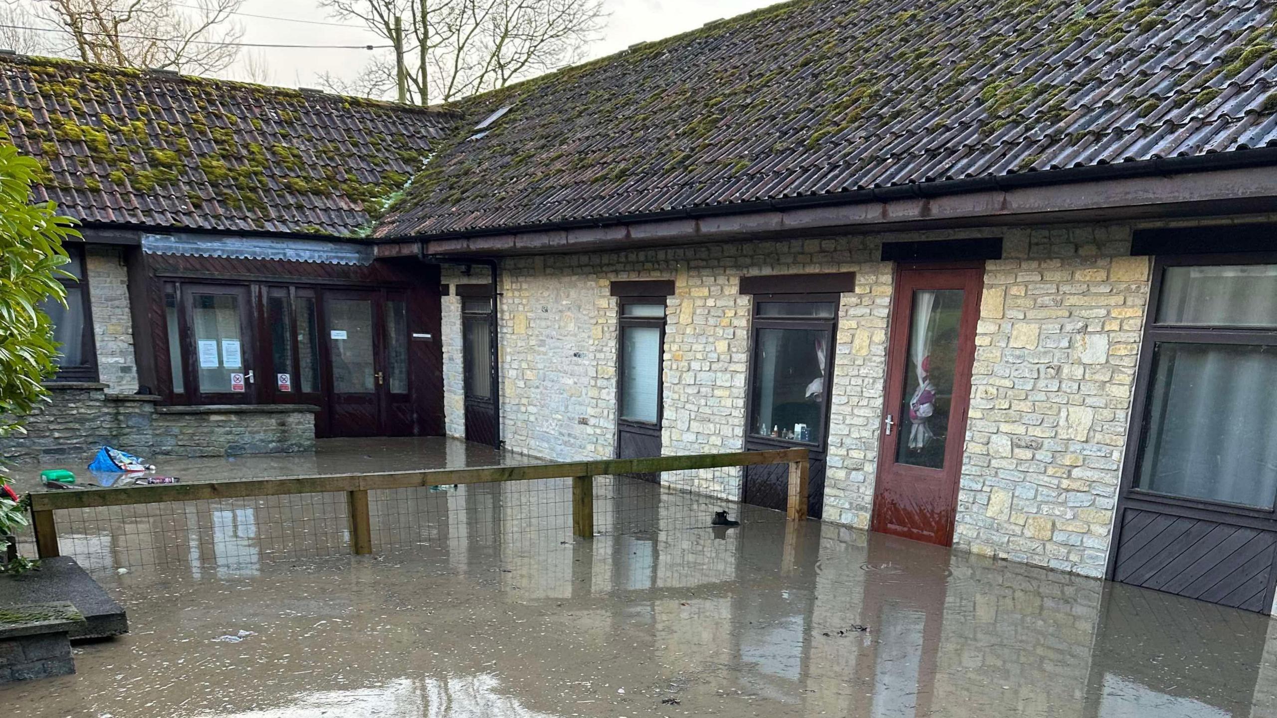 The picture shows the exterior of a one-storey building damaged by muddy floodwater.