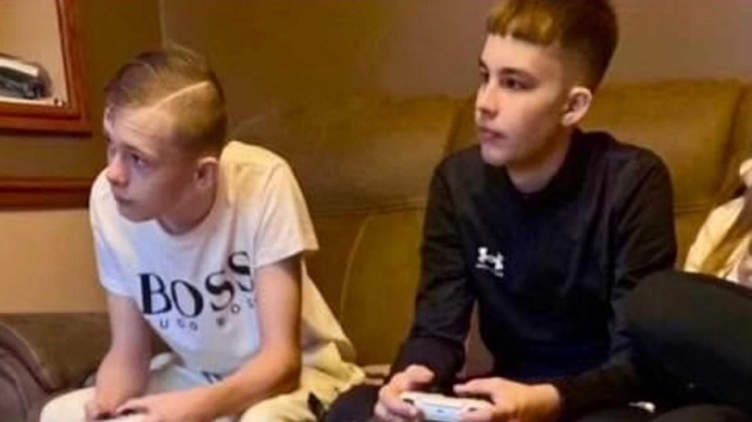 Mason Rist and Max Dixon are pictured sitting on a sofa holding PlayStation controllers and looking at a screen