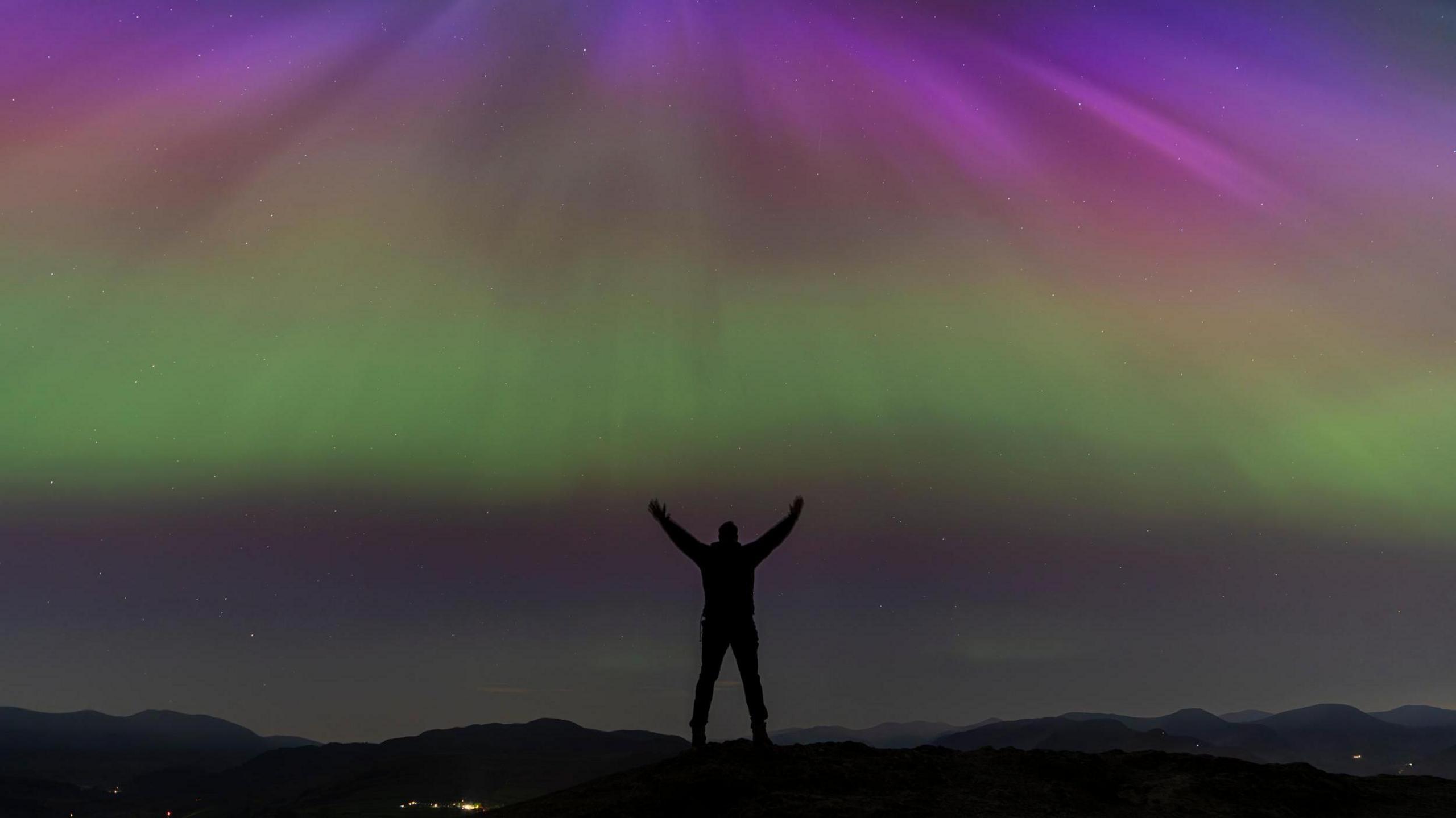 A man on a hilltop with the lights beyond