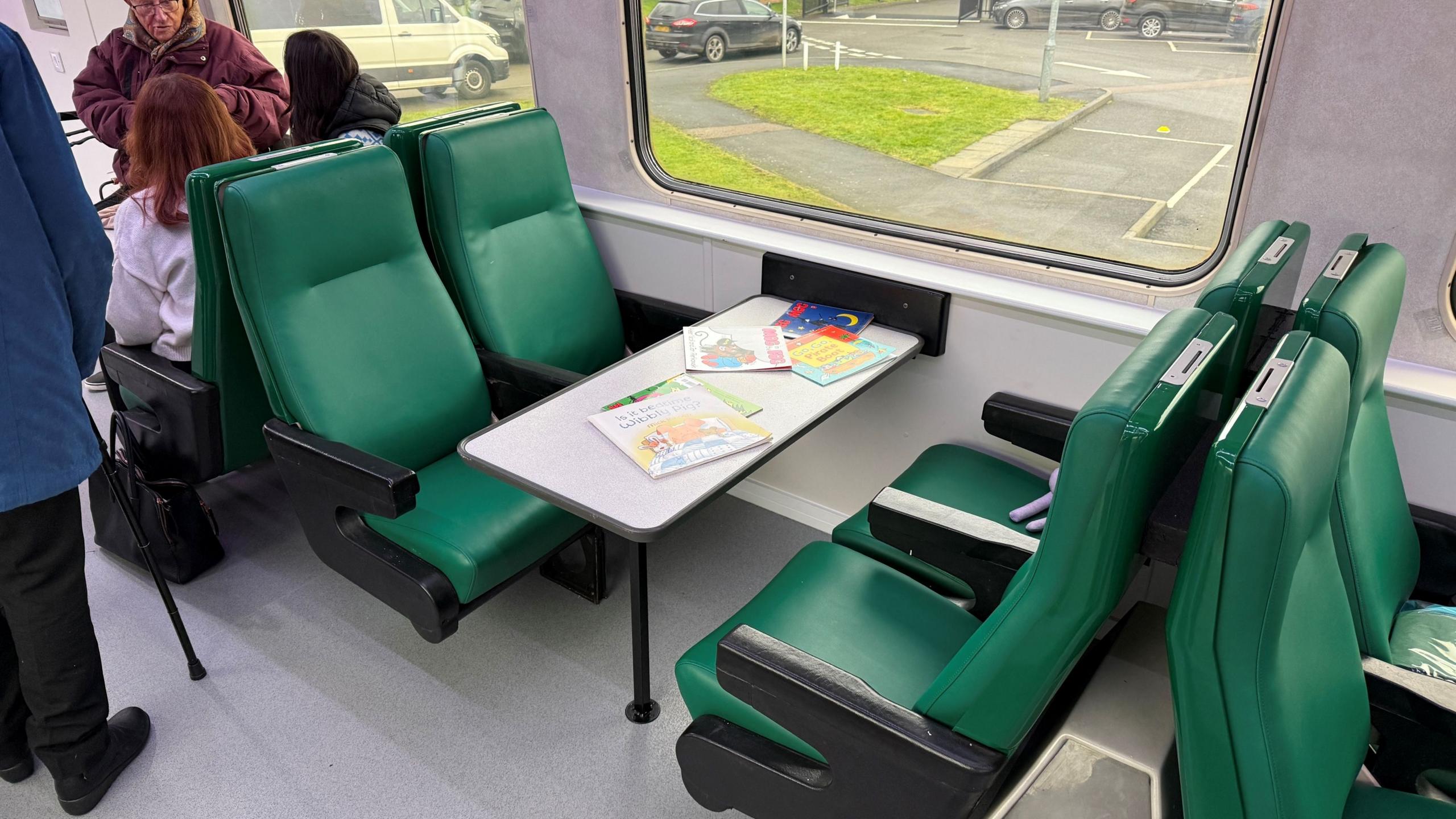 A table and four green chairs inside a train carriage.