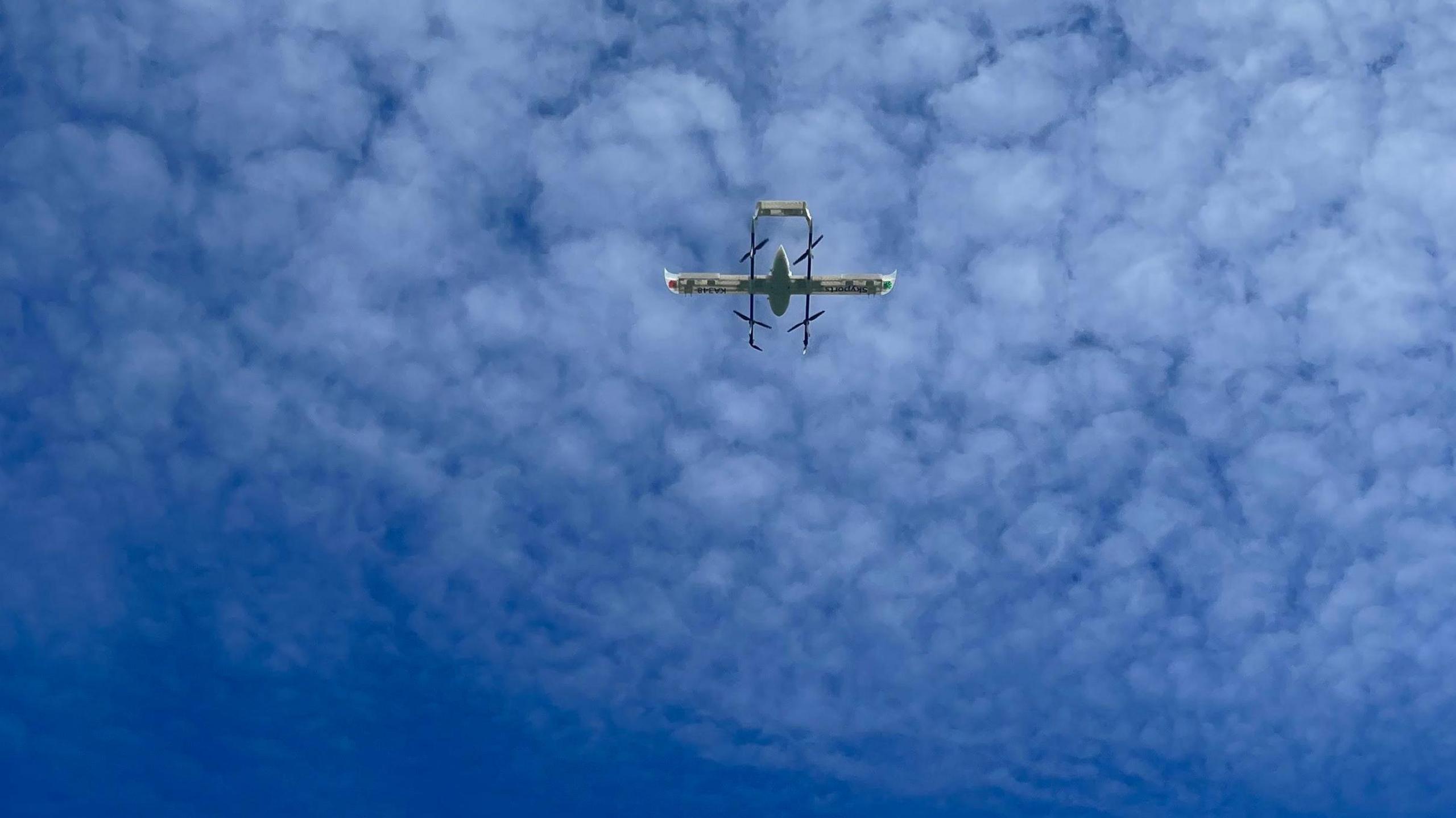 A drone high in the sky with blue sky and light clouds above it 