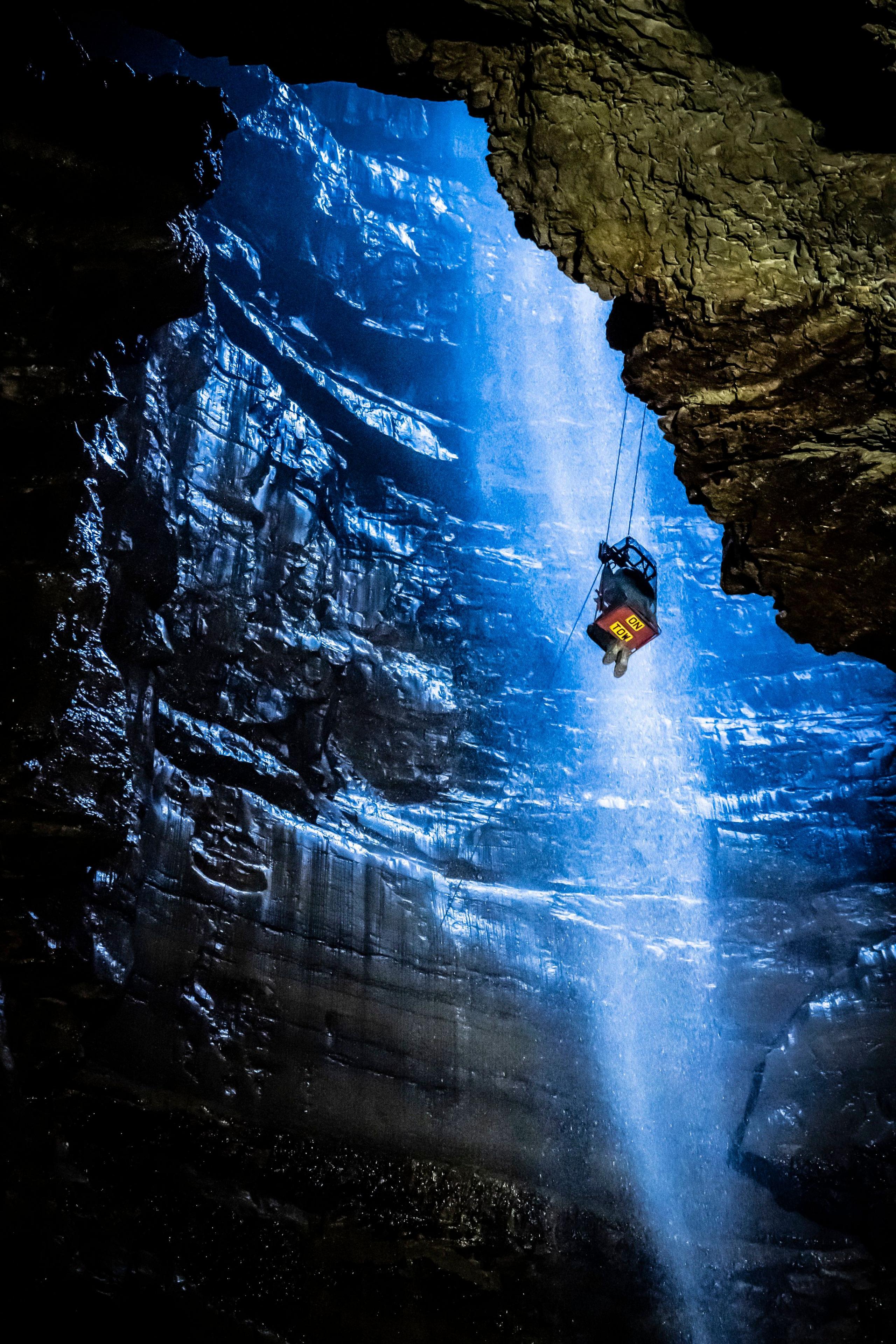 a deep cave with a person sitting on a device that is lowering them into it