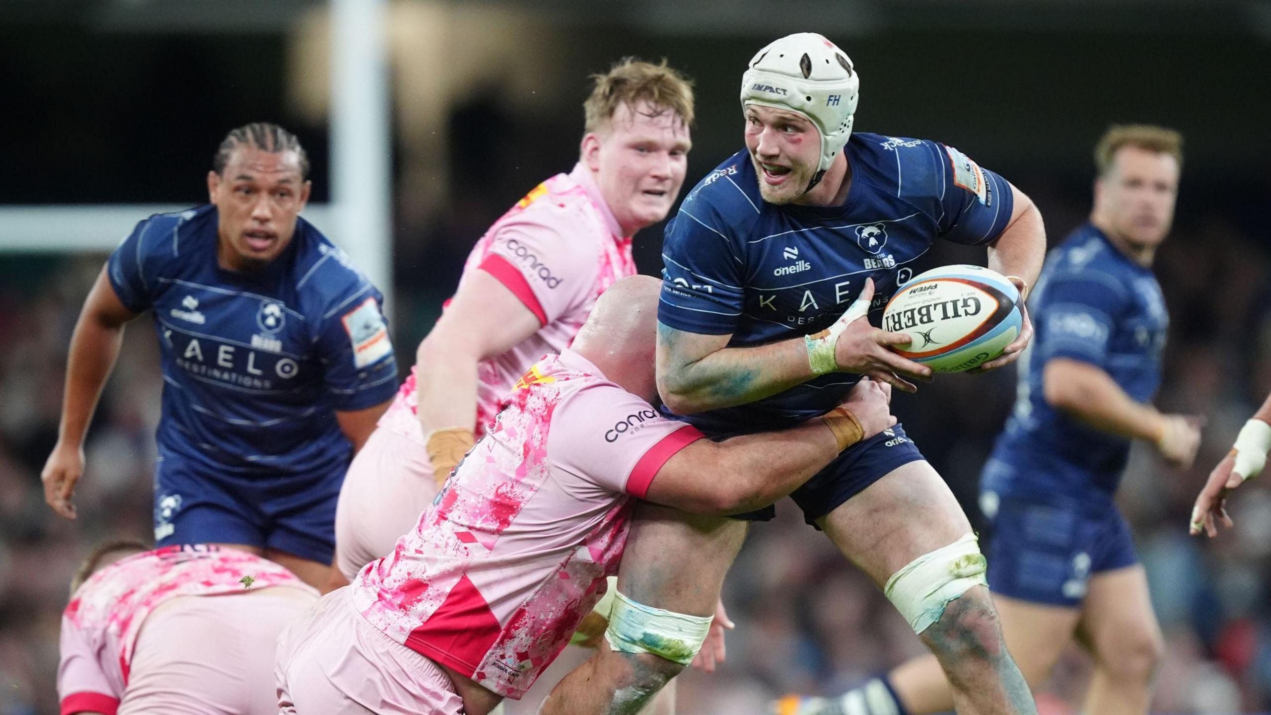 Fitz Harding (right) holds the ball to his side in two hands as a Harlequins player dives and wraps his arms around his middle in a tackle