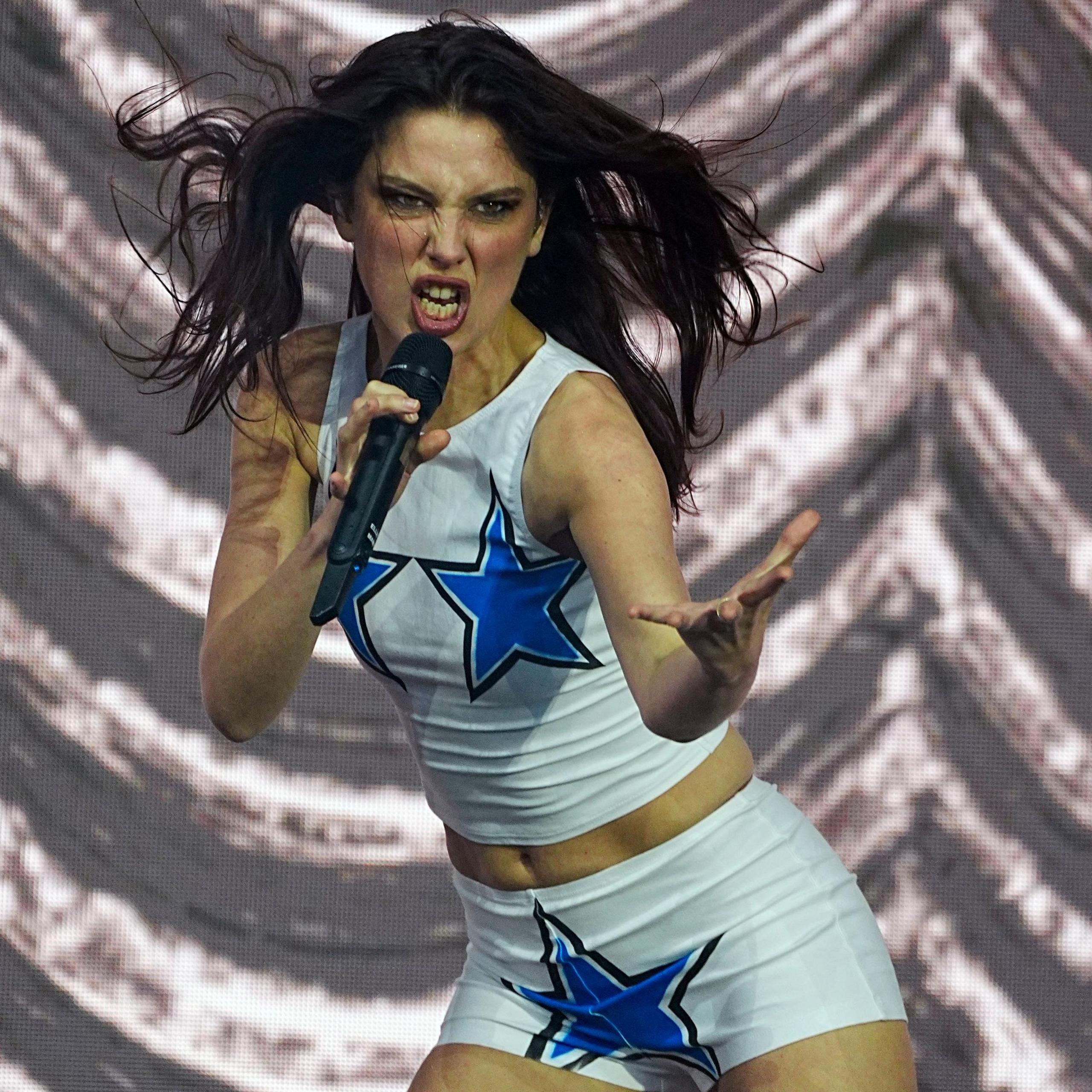 Ellie Rowsell of Wolf Alice plays at the 2025 Glastonbury festival. She is reaching an arm towards the audience while her hair blows in the wind.