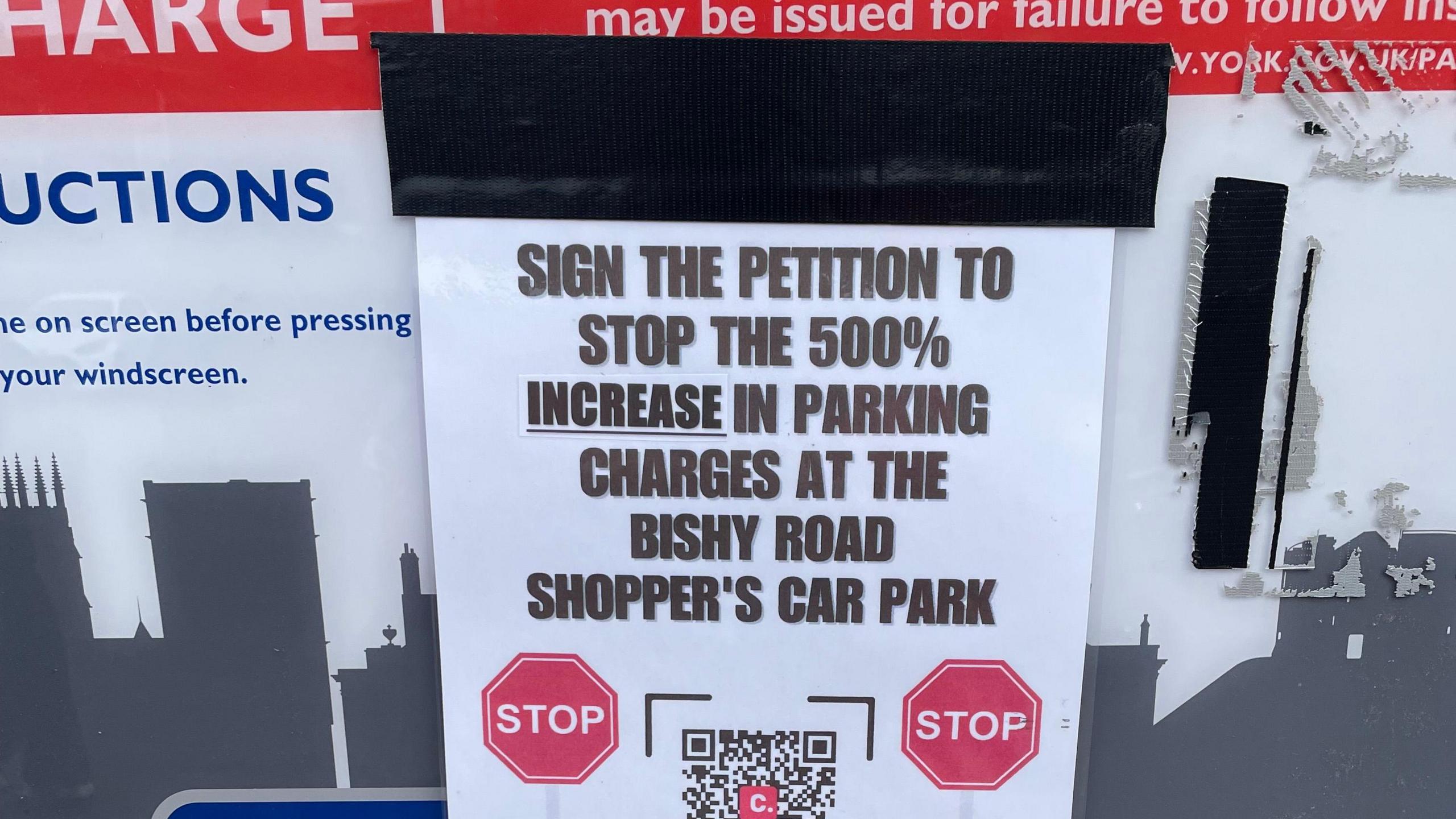 A sign fixed to a car parking charge sign on Bishopthorpe Road, York. It urges a rethink over increased charges and asks people to sign a petition