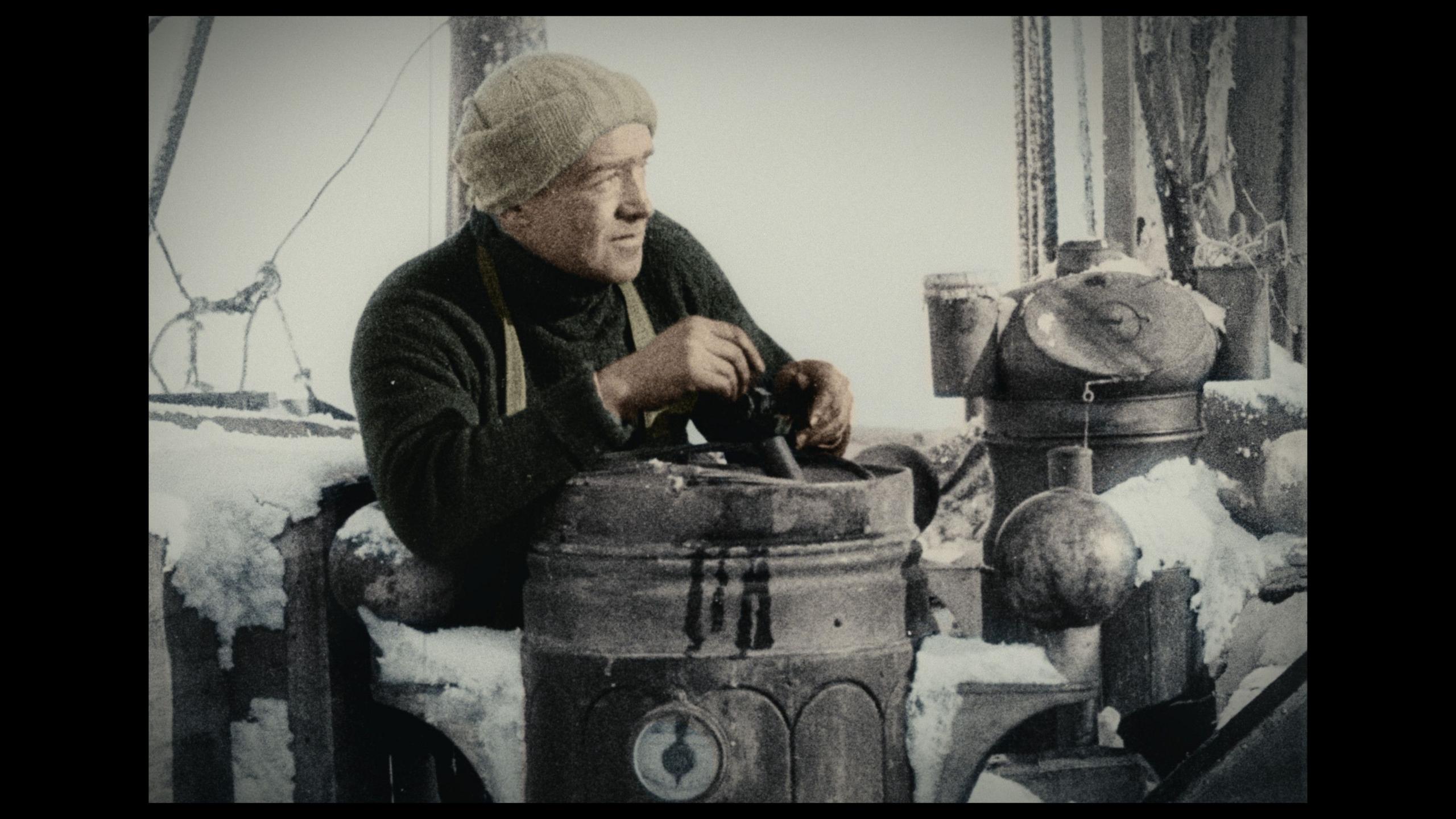 A colour photograph of Sir Ernest Shackleton on deck surrounded by ship equipment covered in ice