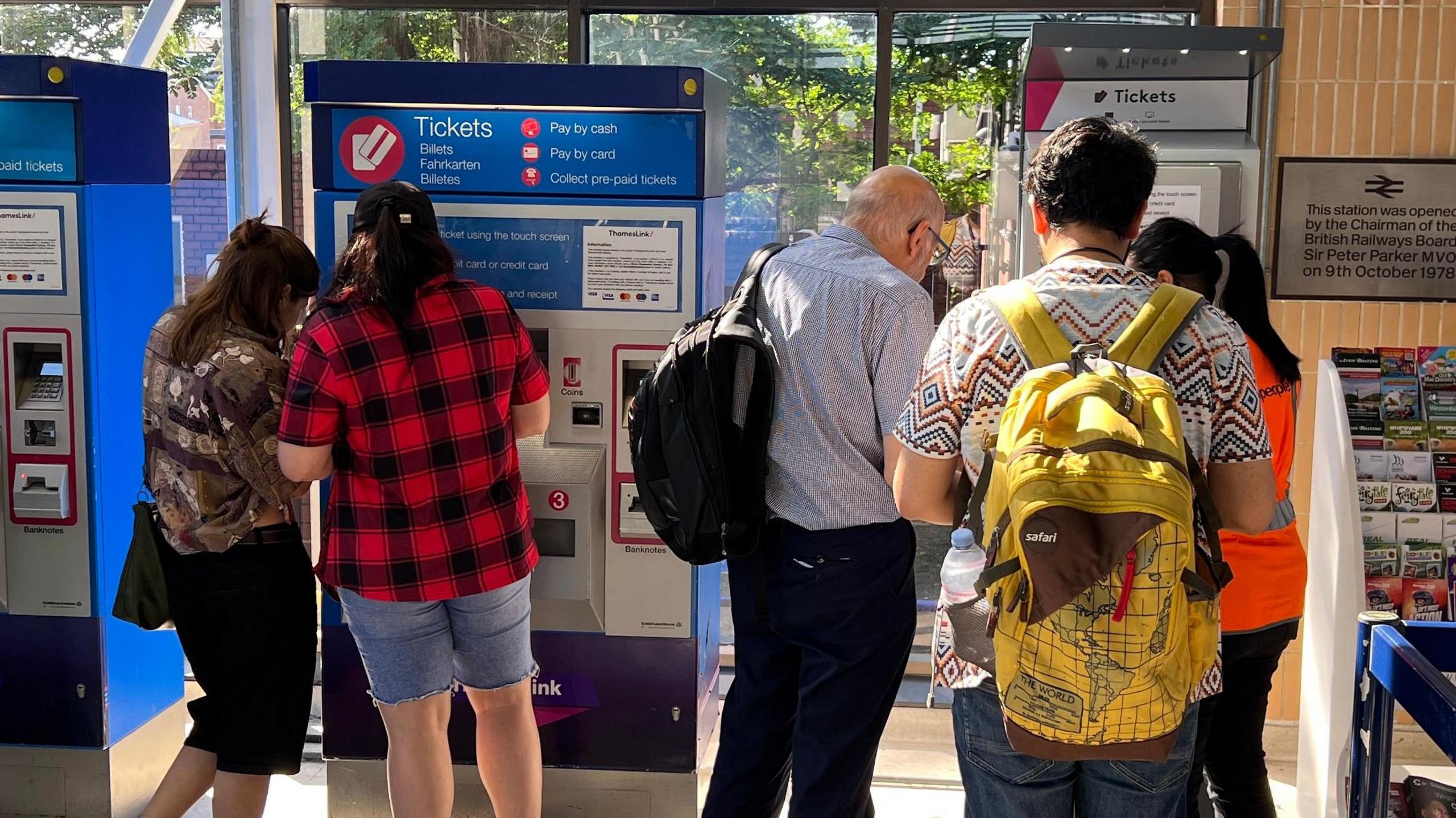 Customers in summer clothing buy tickets at two self-service machines in a station