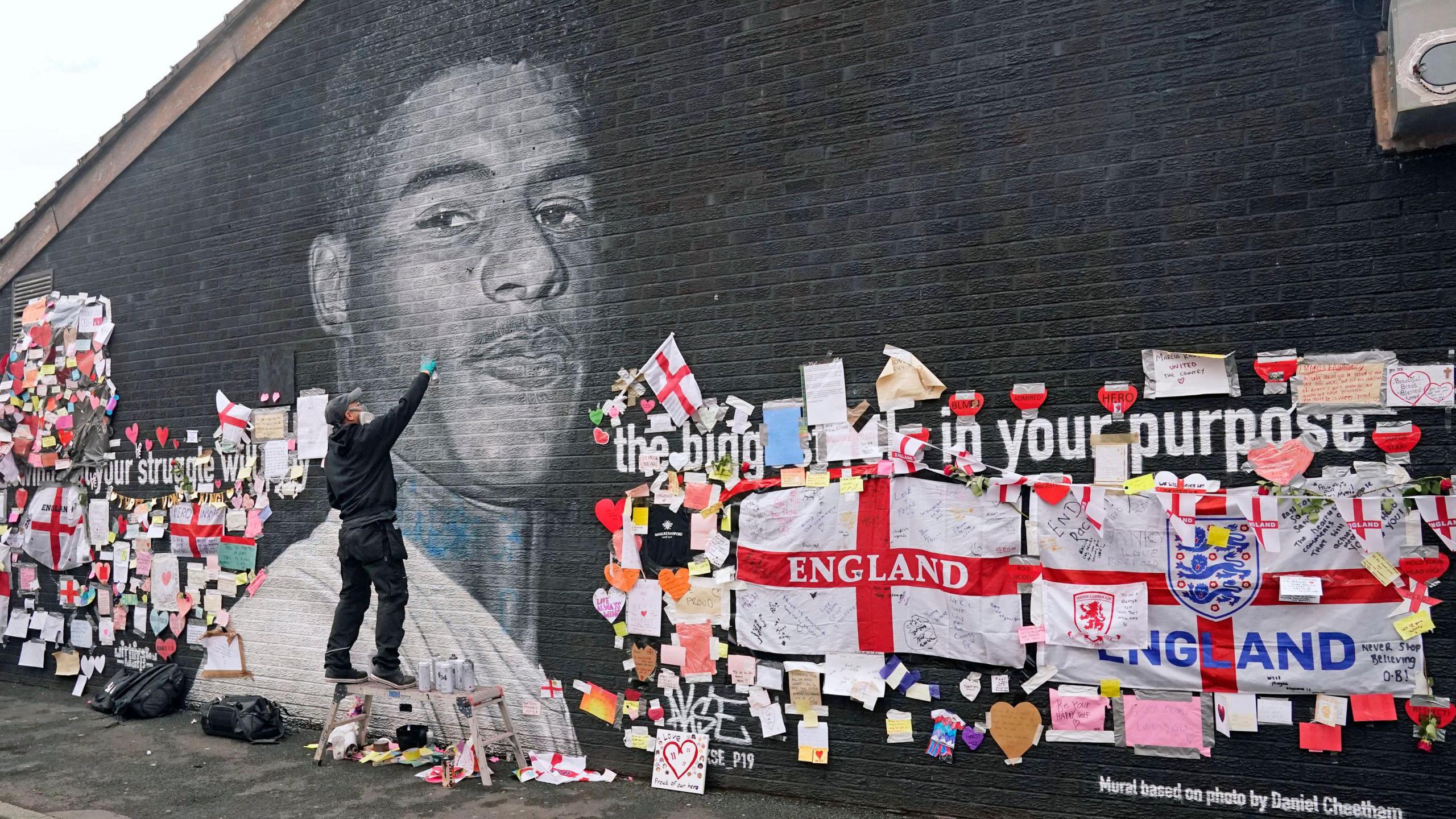 Street artist Akse P19 repairs the mural of Manchester United striker and England player Marcus Rashford on the wall of the Coffee House Cafe on Copson Street, Withington