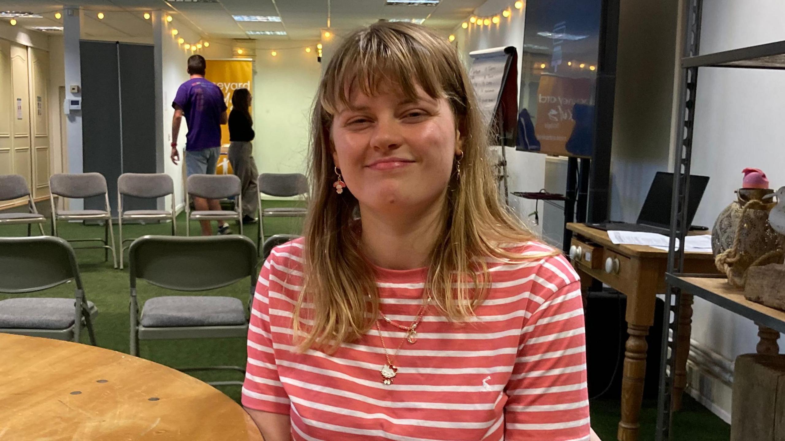 A woman with shoulder length blonde and brown hair in a coral and white striped t-shirt.
