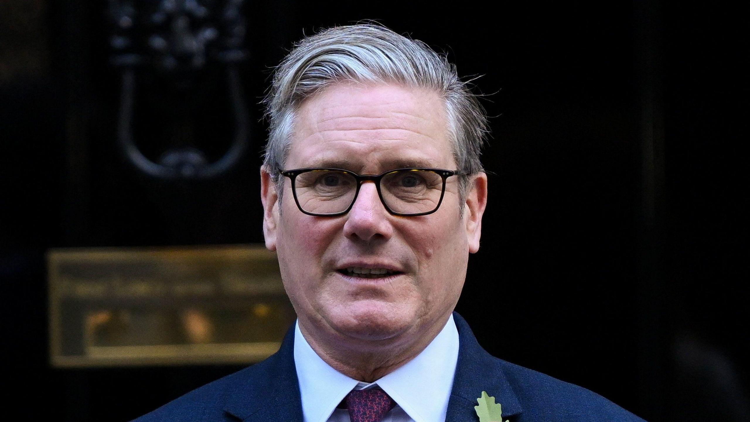 Prime Minister Sir Keir Starmer, pictured from the shoulders up. he is wearing glasses a blue shirt, purple tie and navy suit.