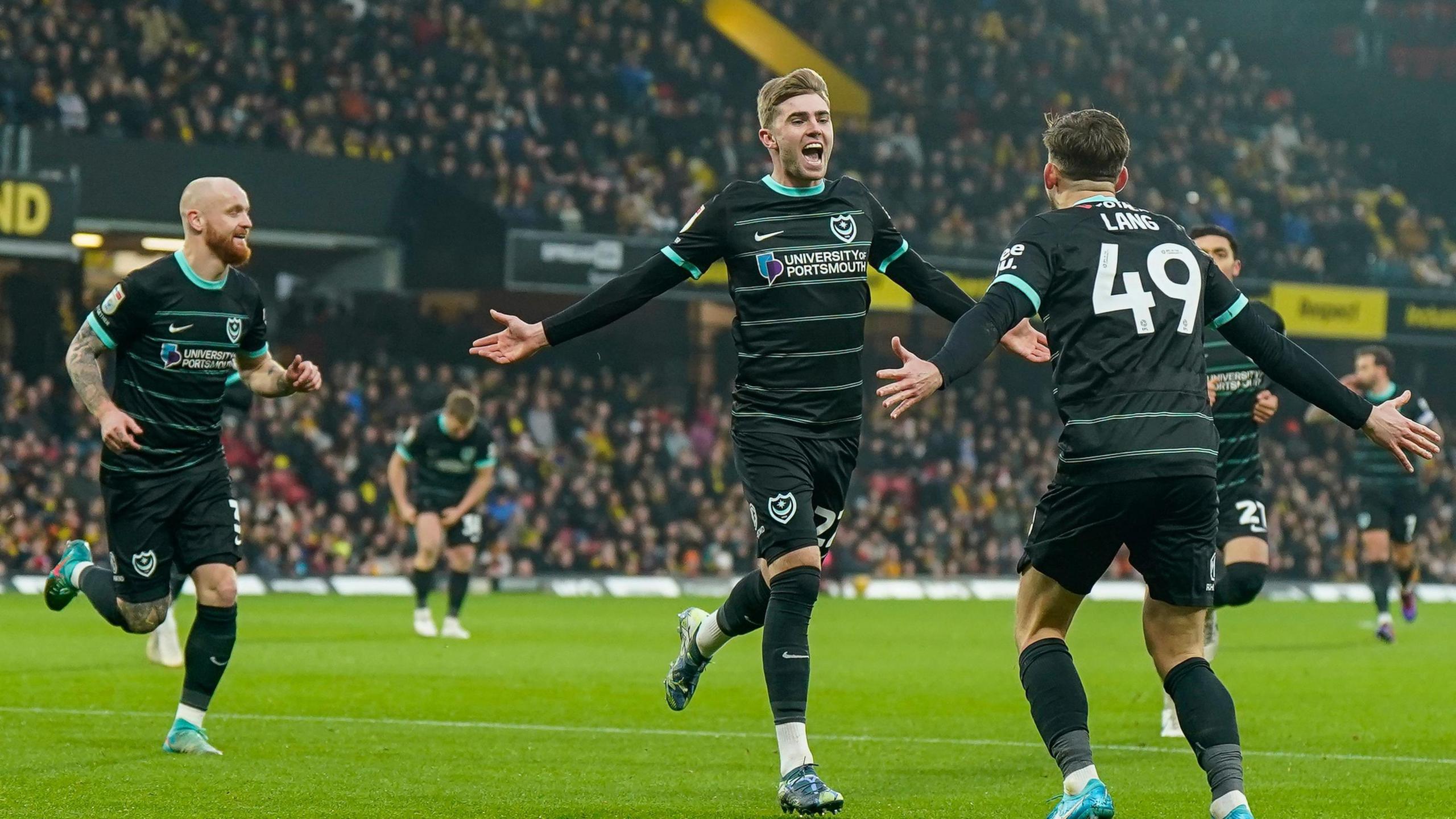 Zak Swanson celebrates with his arms out wide along with teammate Callum Lang after scoring for Portsmouth against Watford.