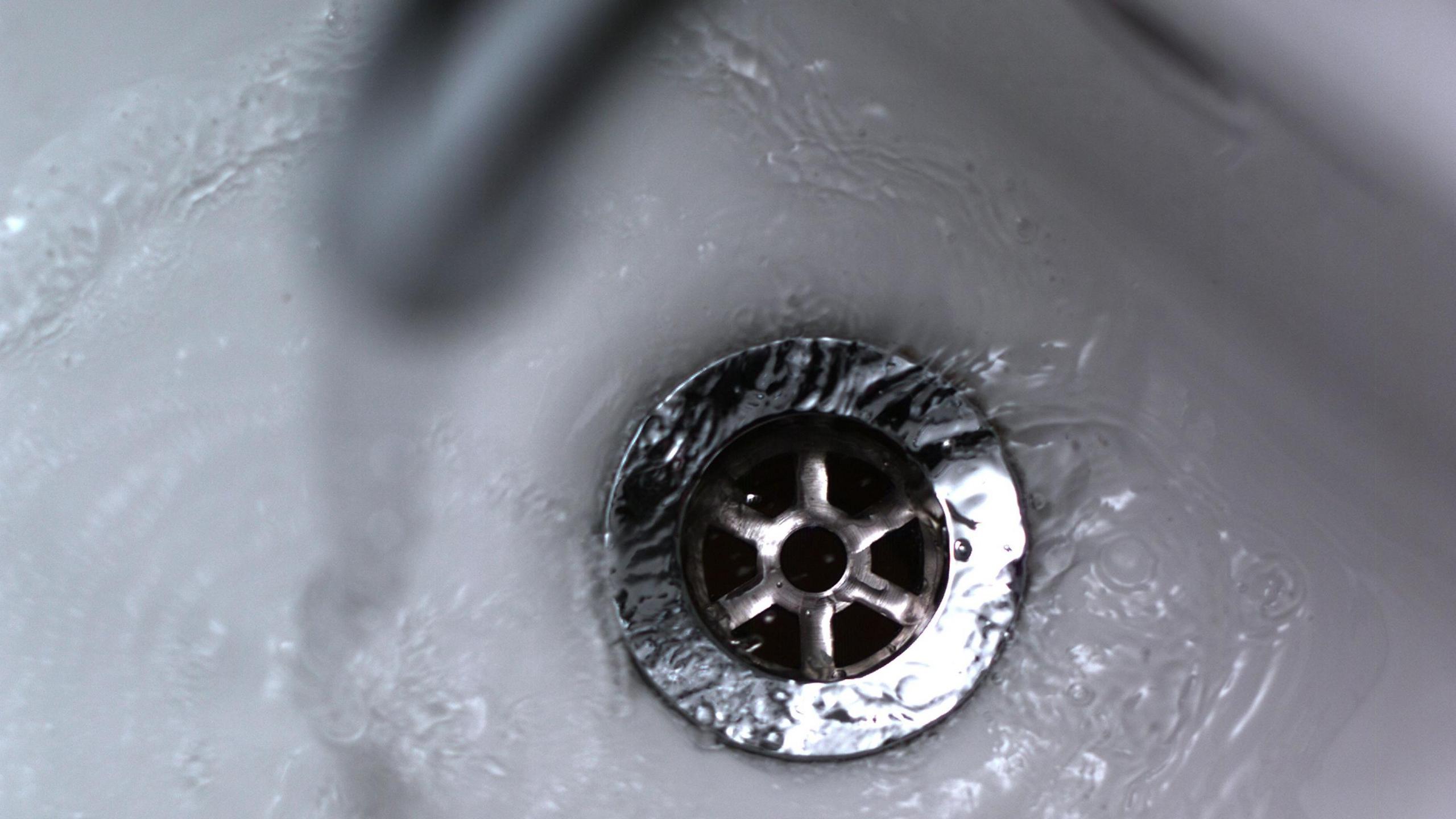 A close up picture of water draining down the plughole of a white sink