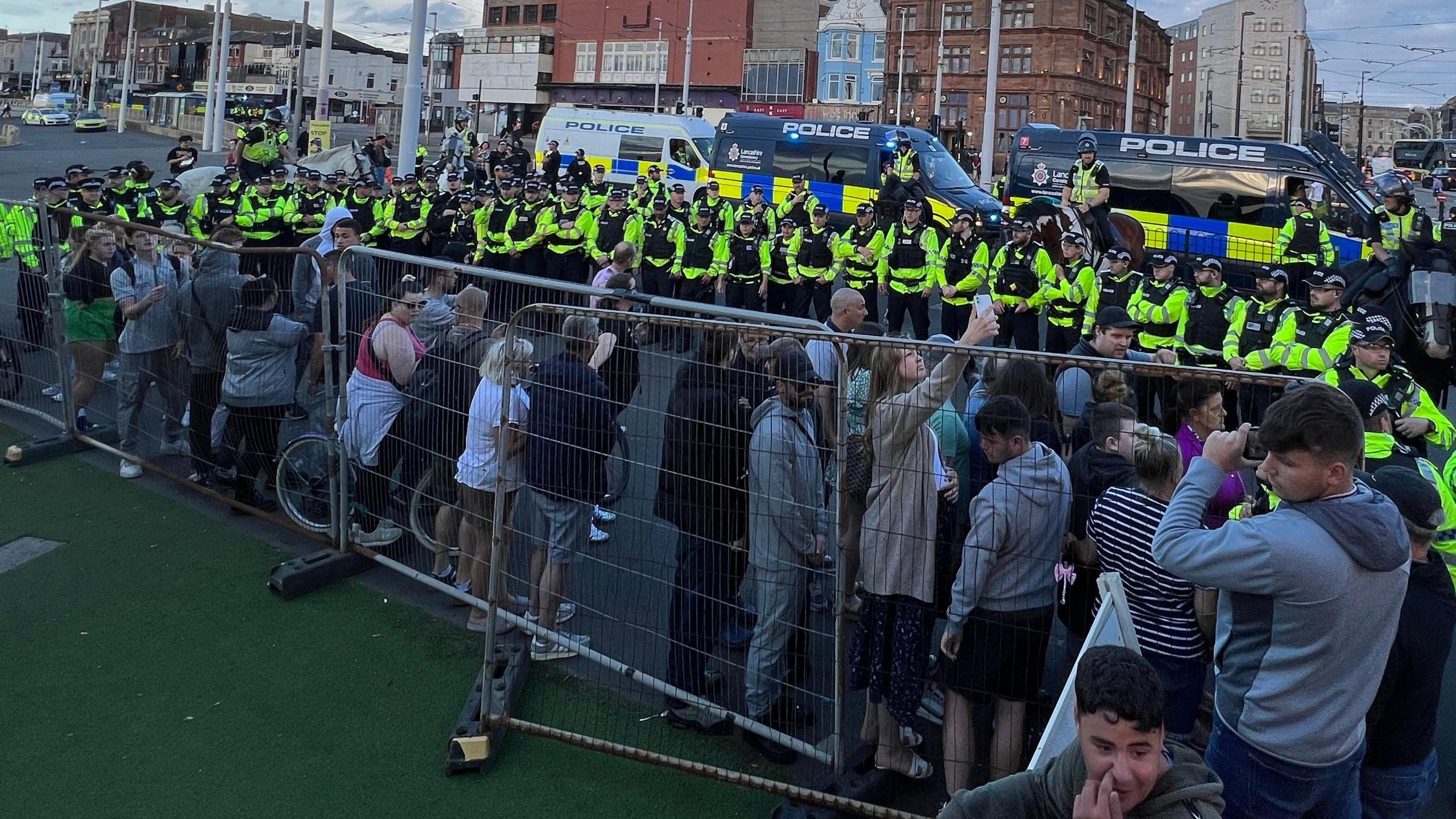 A group of protesters stand alongside a fence after being kettled by a line of police officers in hi-vis jackets