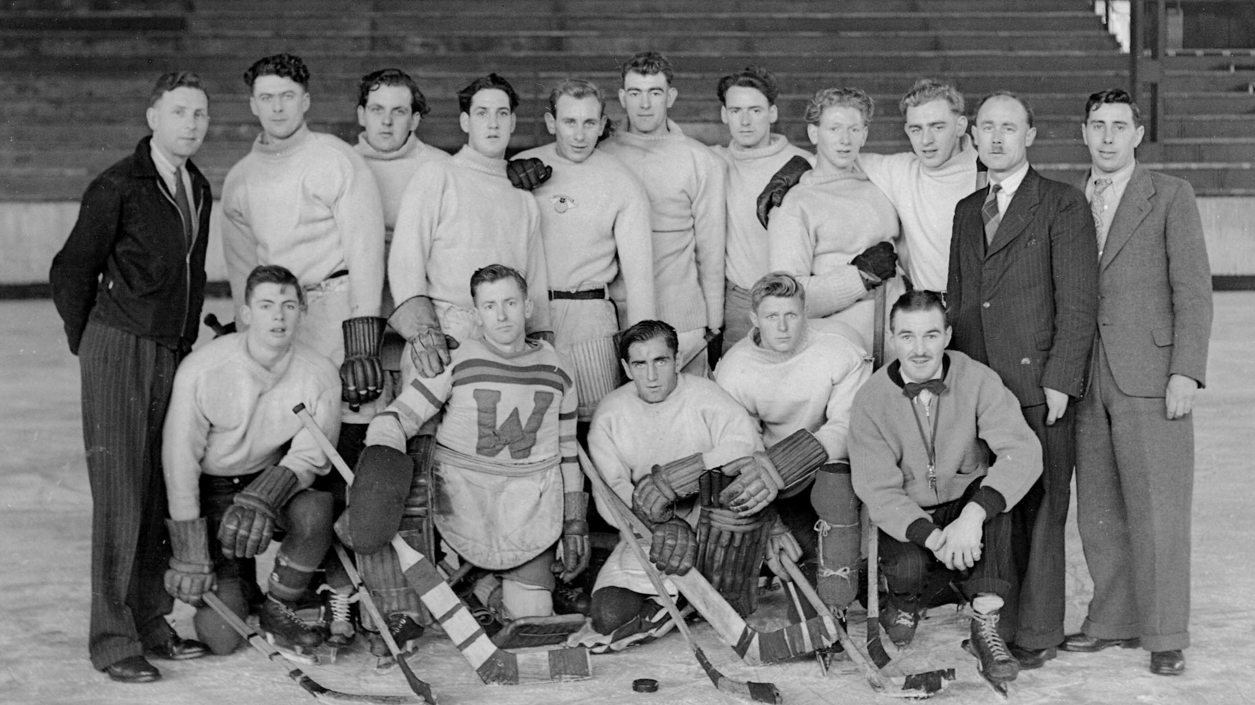 A black and white group photograph of Durham Wasps ice hockey team at Durham Ice Rink, October 1947. Russ Proudfoot is standing the back, third person from left to right. He has black wavy hair and is wearing a white jumper.