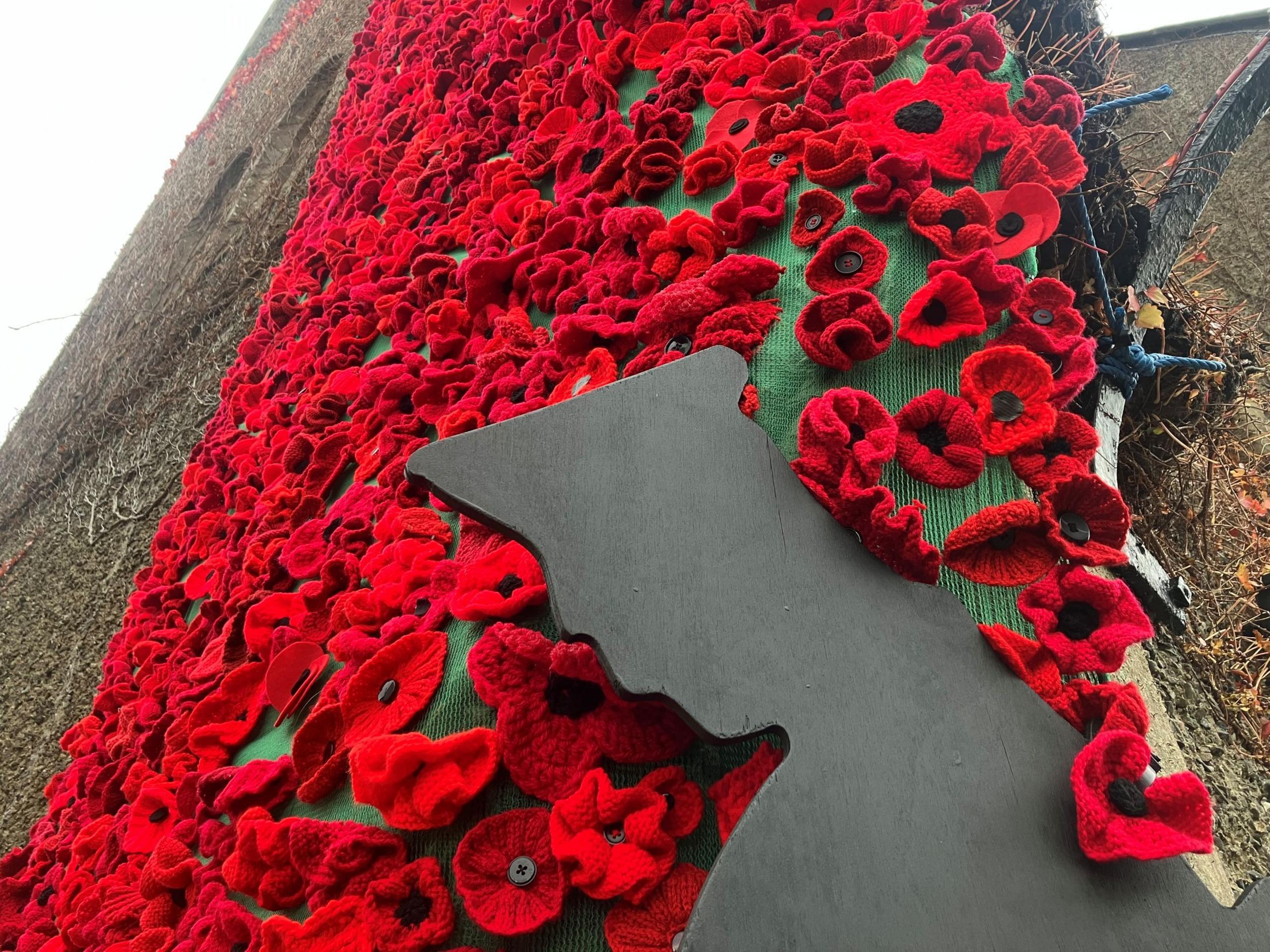 Hand-knitted poppies on the exterior wall of a church, there is also a black silhouette of a soldier.