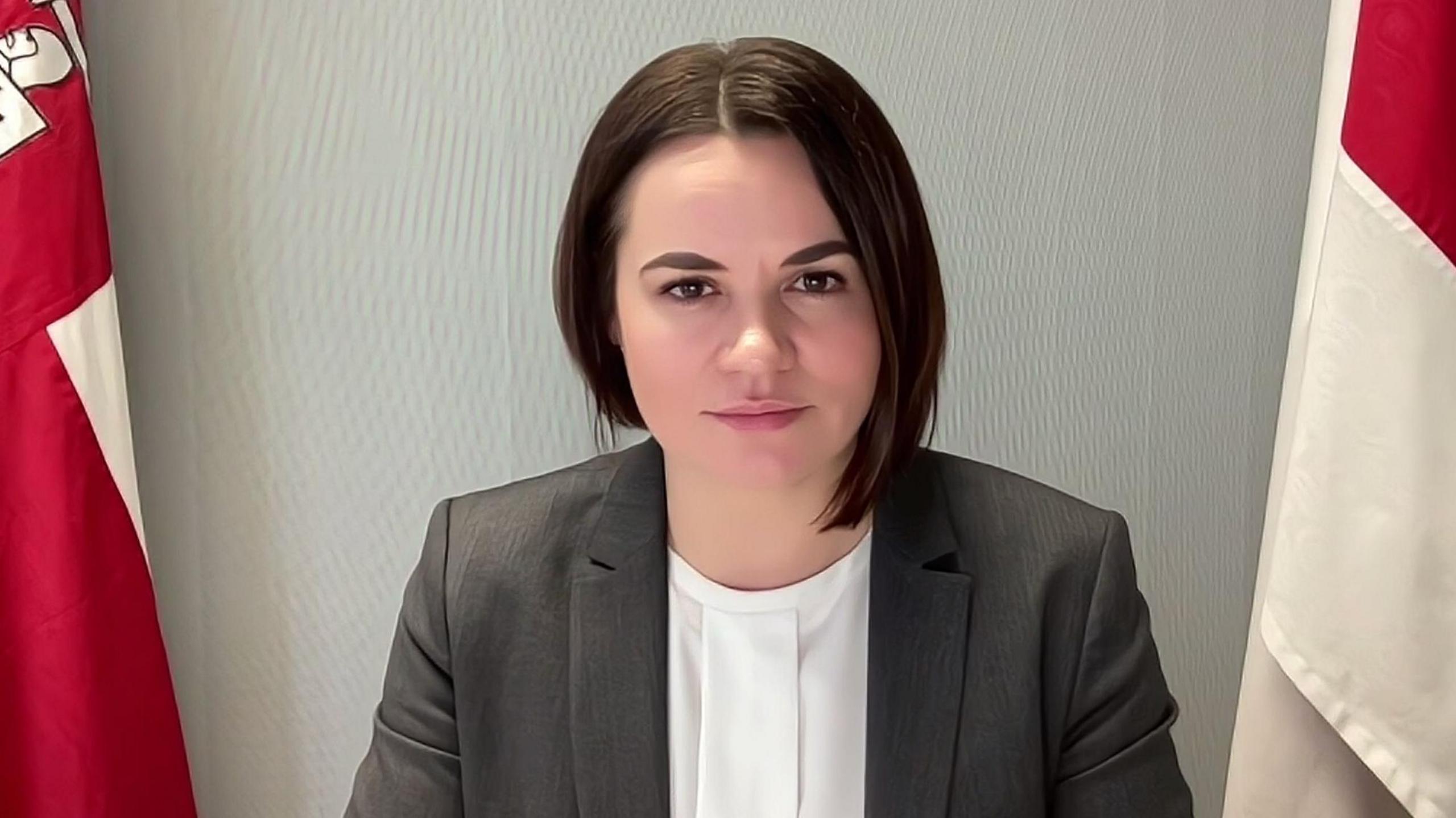 Svetlana Tikhanovskaya sits between two flags for a videocall.