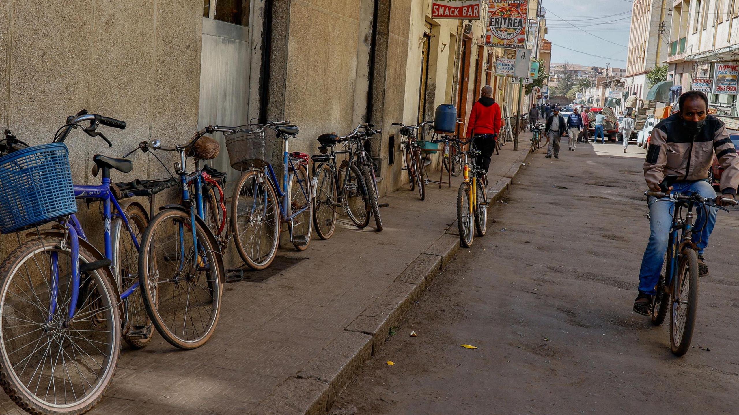 Bicycles are leant against a wall on a busy street in Asmara, Eritrea, as a man rides down the road towards the camera