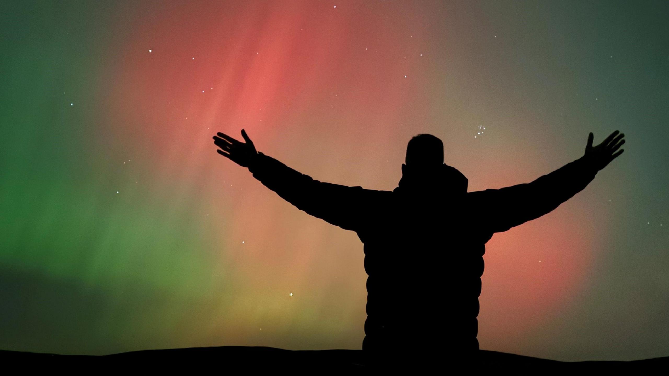 back of a man with arms held aloft while looking at ripples of green and red over Lancashire hills