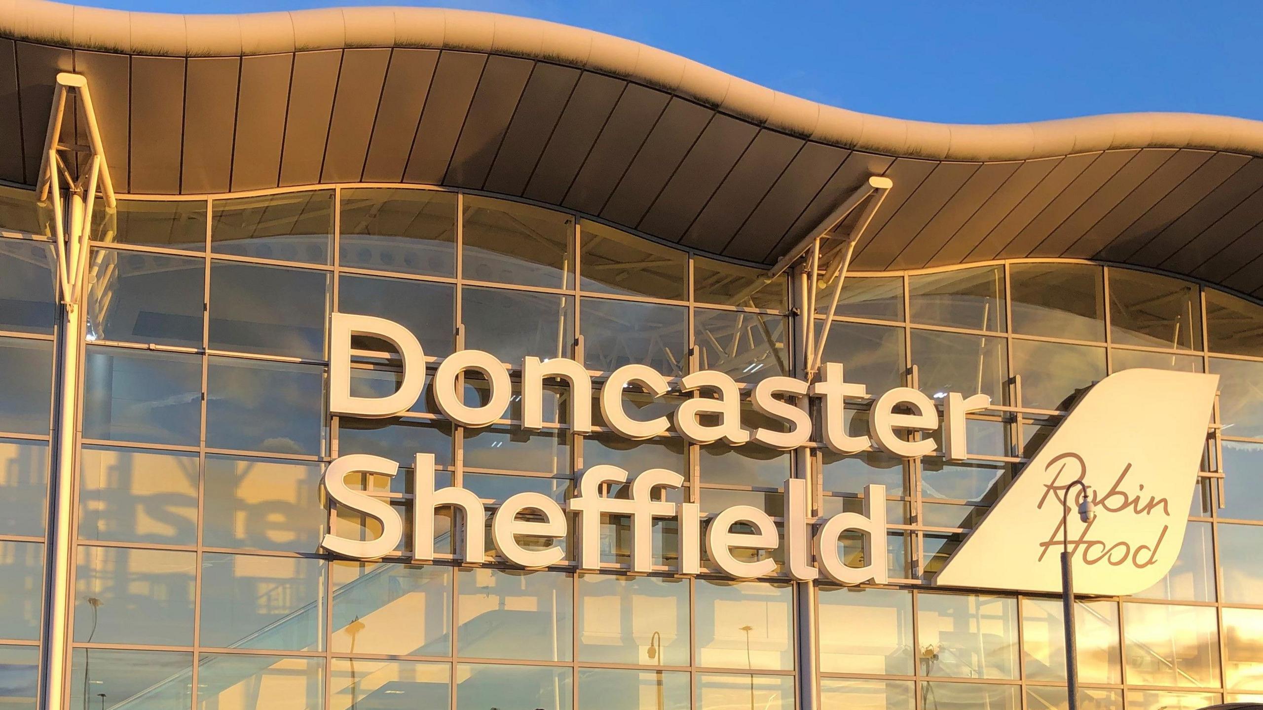 A sign saying Doncaster Sheffield Airport on the outside of a steal and glass airport terminal building.