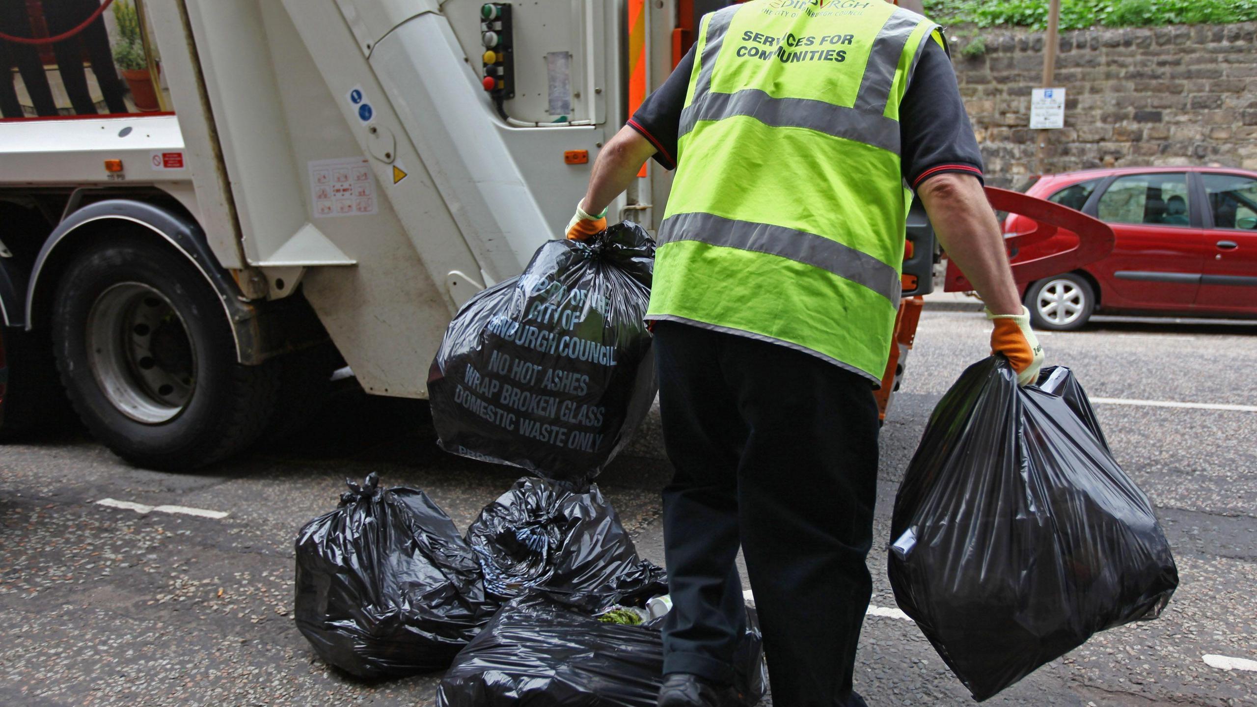 A waste worker carrying bags to a truck