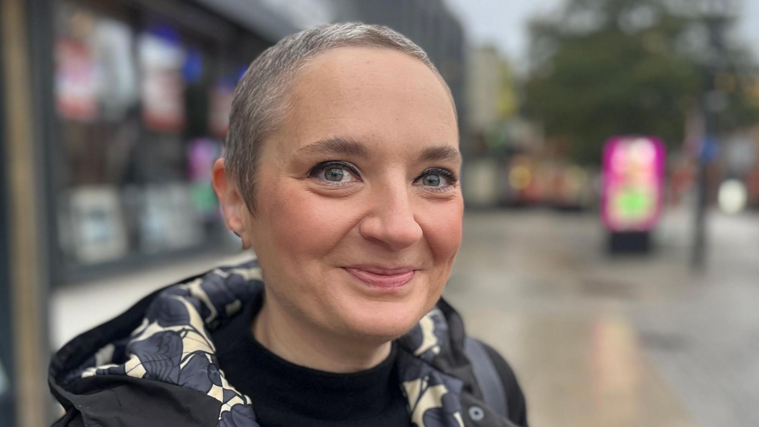 Lucy Shannon is standing on the high street and smiling at the camera. She has short grey hair.