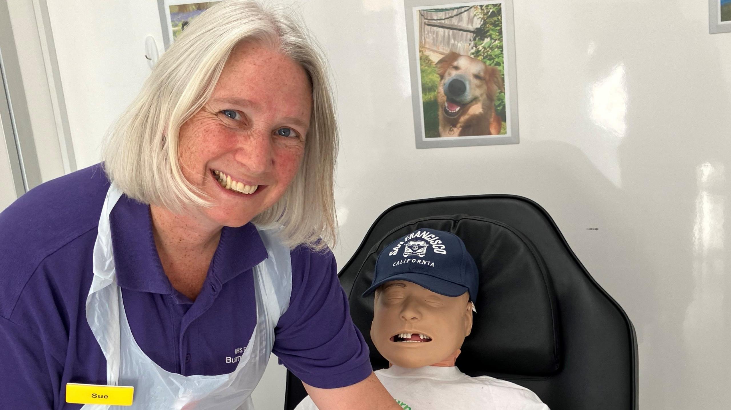 A woman in an apron smiling while leaning over a dummy