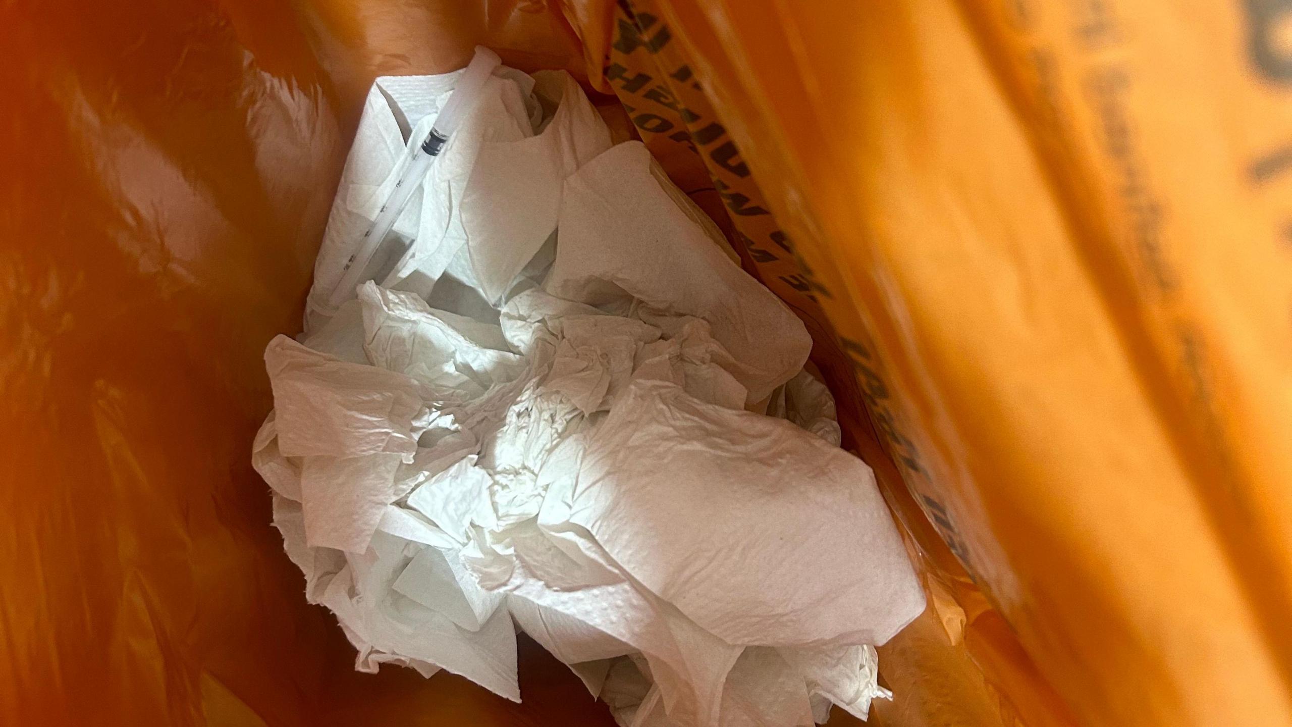 A used needle sitting on top of hand towels inside an orange bag