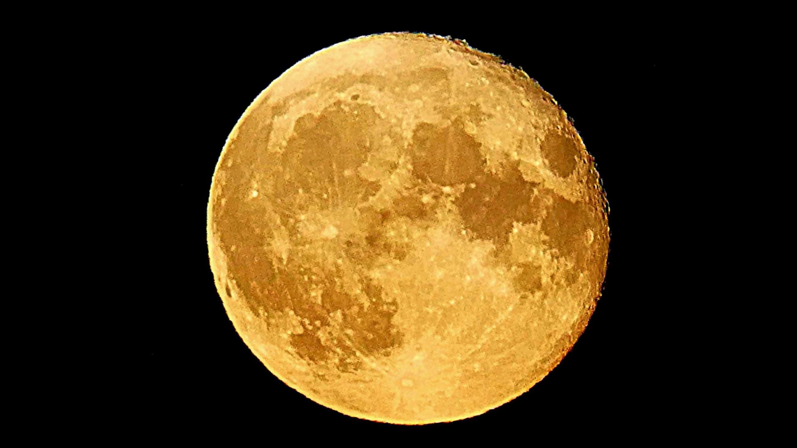 A full moon in a black night sky it is golden in colour and its surface is clearly visible.